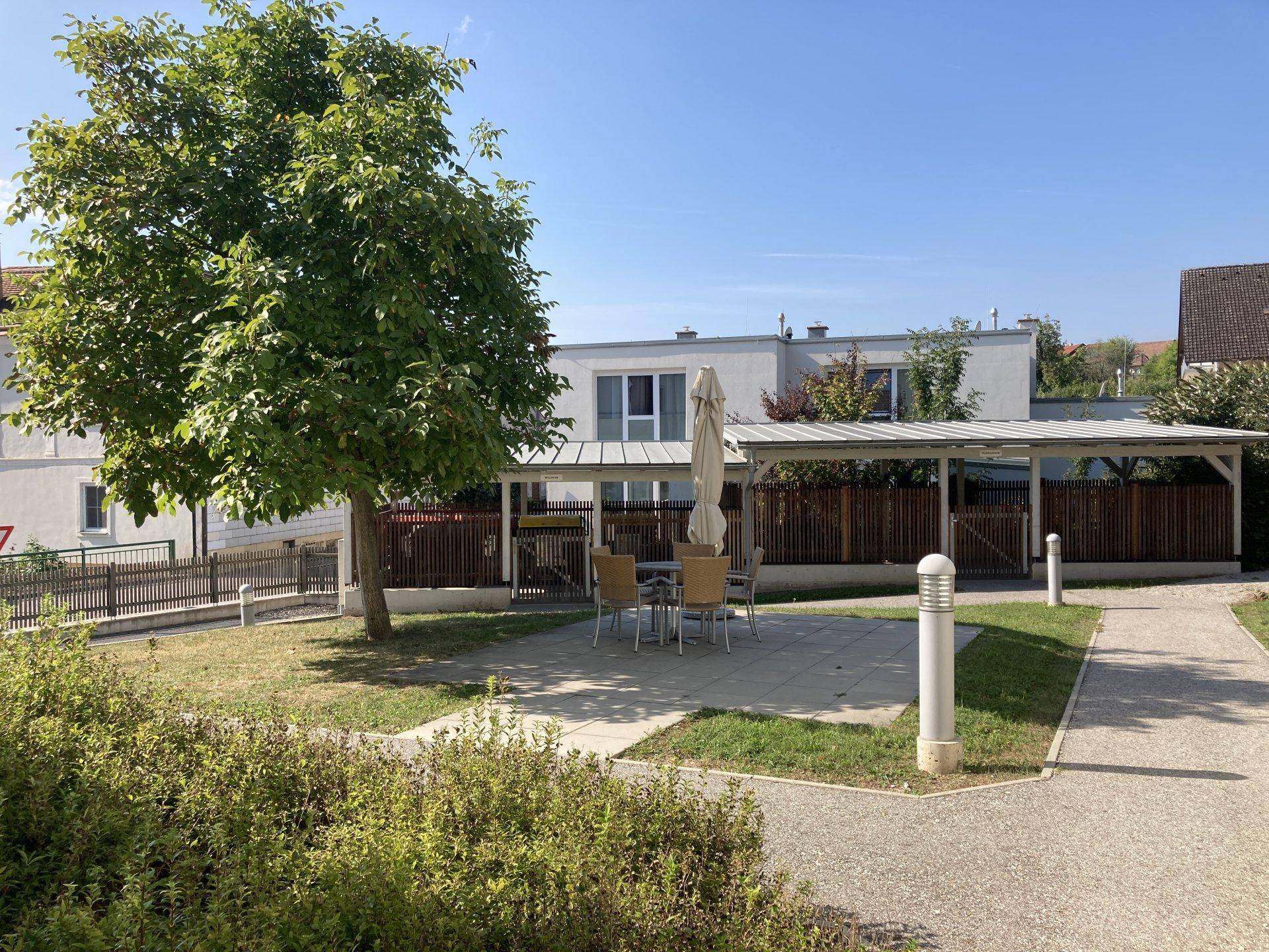 Gartenbereich mit Sitzgelegenheiten und einem überdachten Parkplatz für Fahrzeuge.