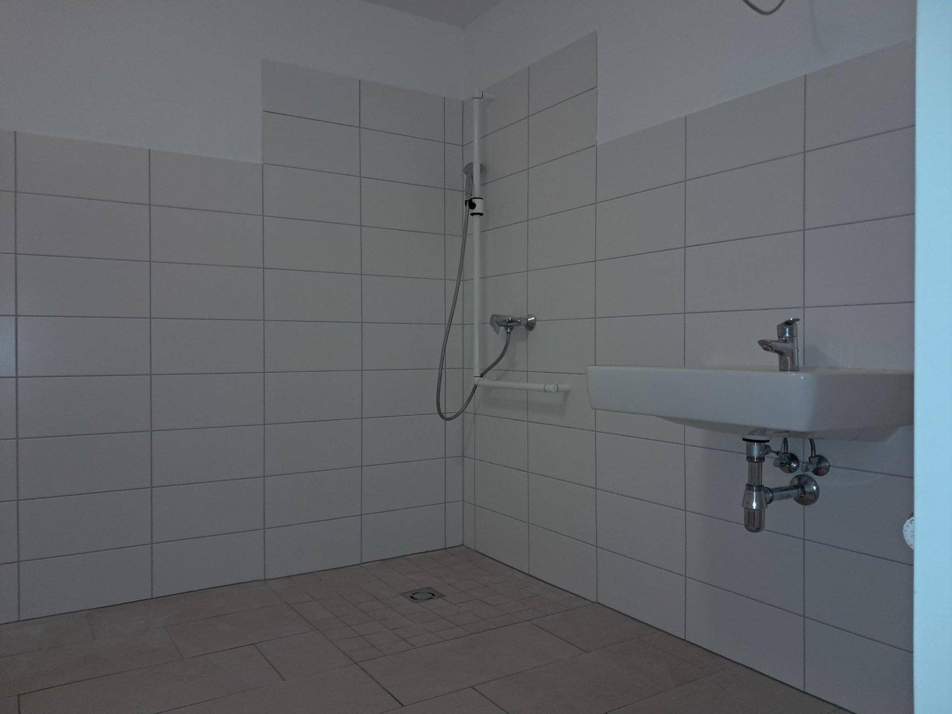 Modernes Badezimmer mit ebenerdiger Dusche, weißen Fliesen und einem Waschbecken.