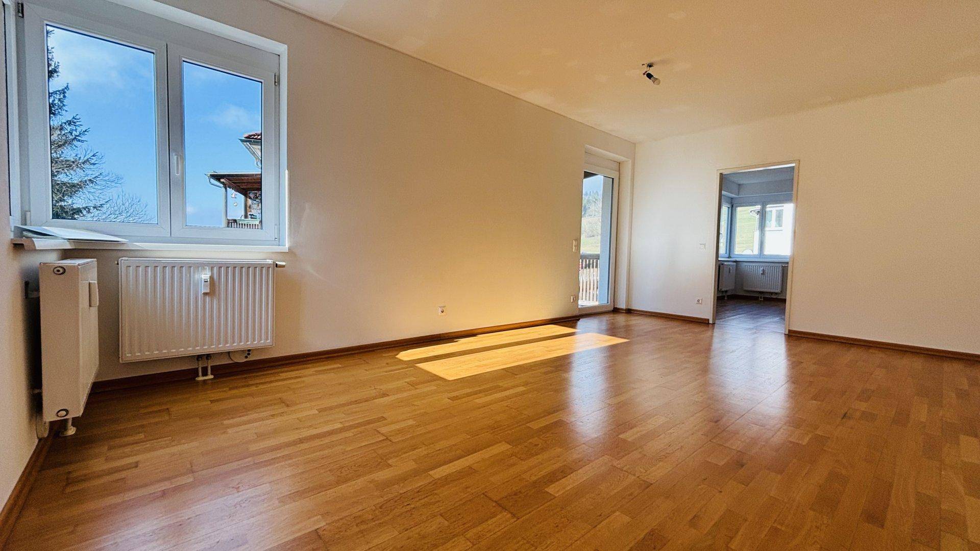 Helles Wohnzimmer mit Parkettboden, großen Fenstern und Zugang zu einem Balkon.