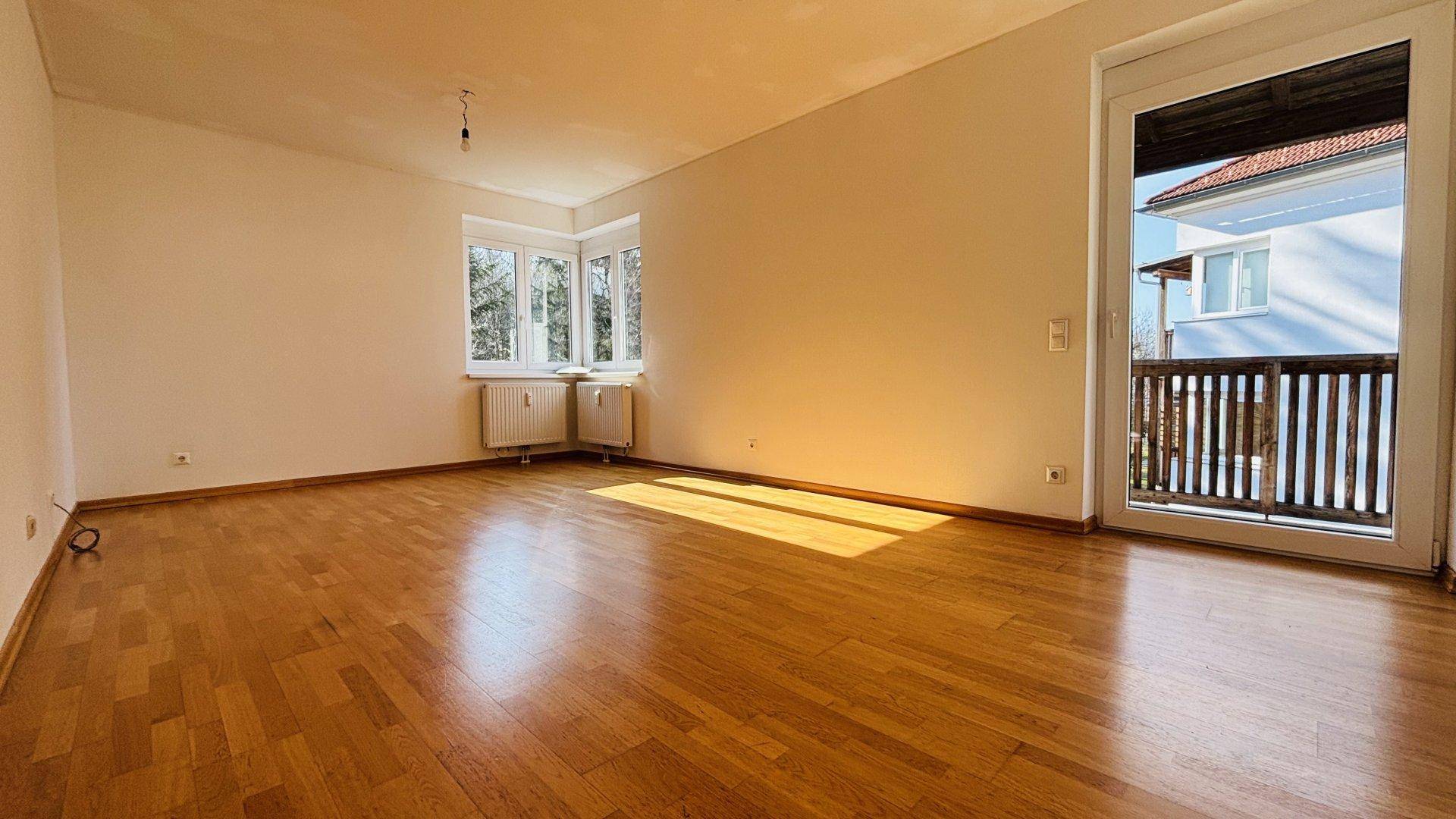 Lichtdurchflutetes Wohnzimmer mit Parkettboden, Erkerfenster und Zugang zum Balkon.