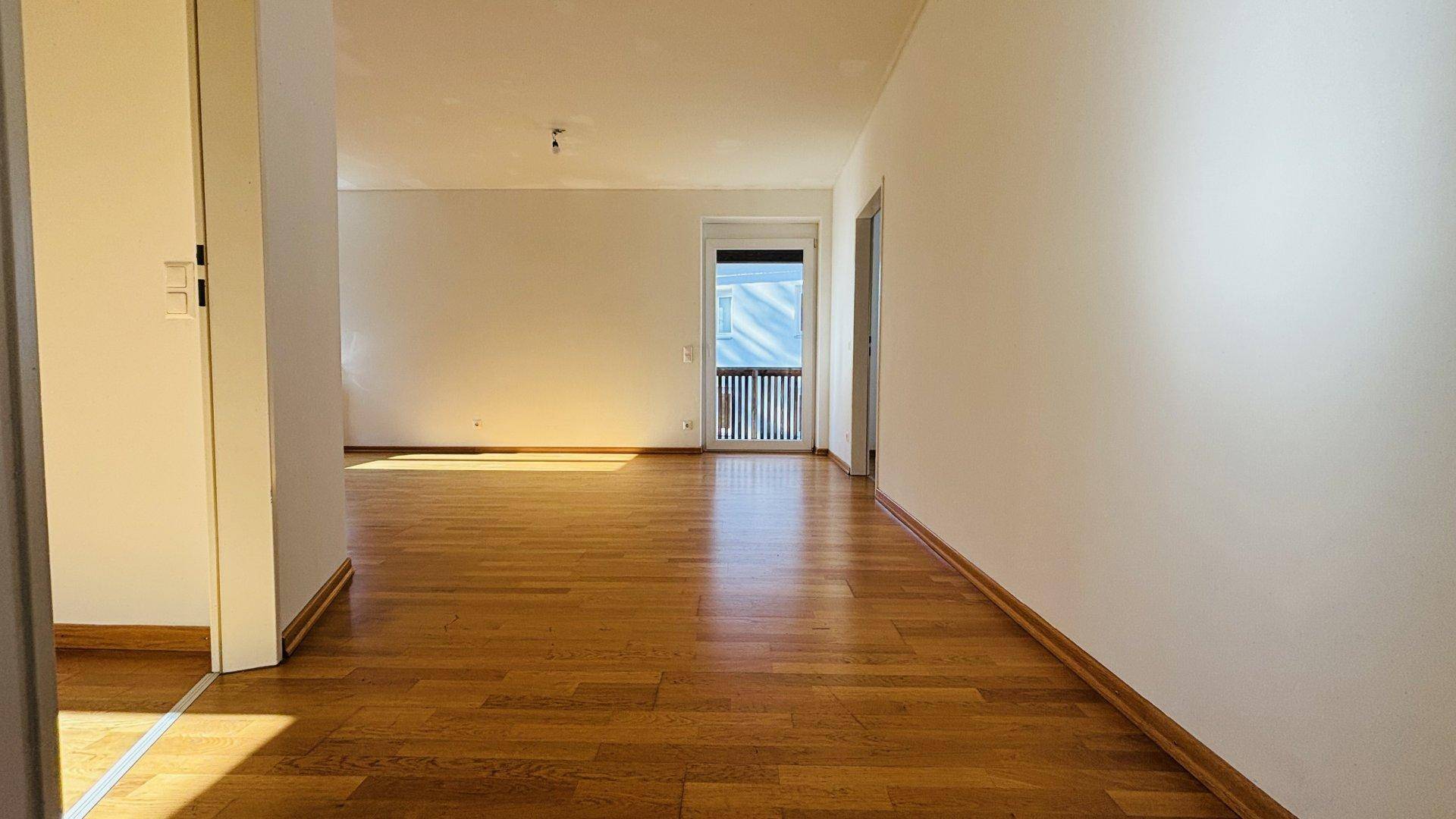 Geräumiges Wohnzimmer mit Holzboden, weiß gestrichenen Wänden und viel natürlichem Lichteinfall.