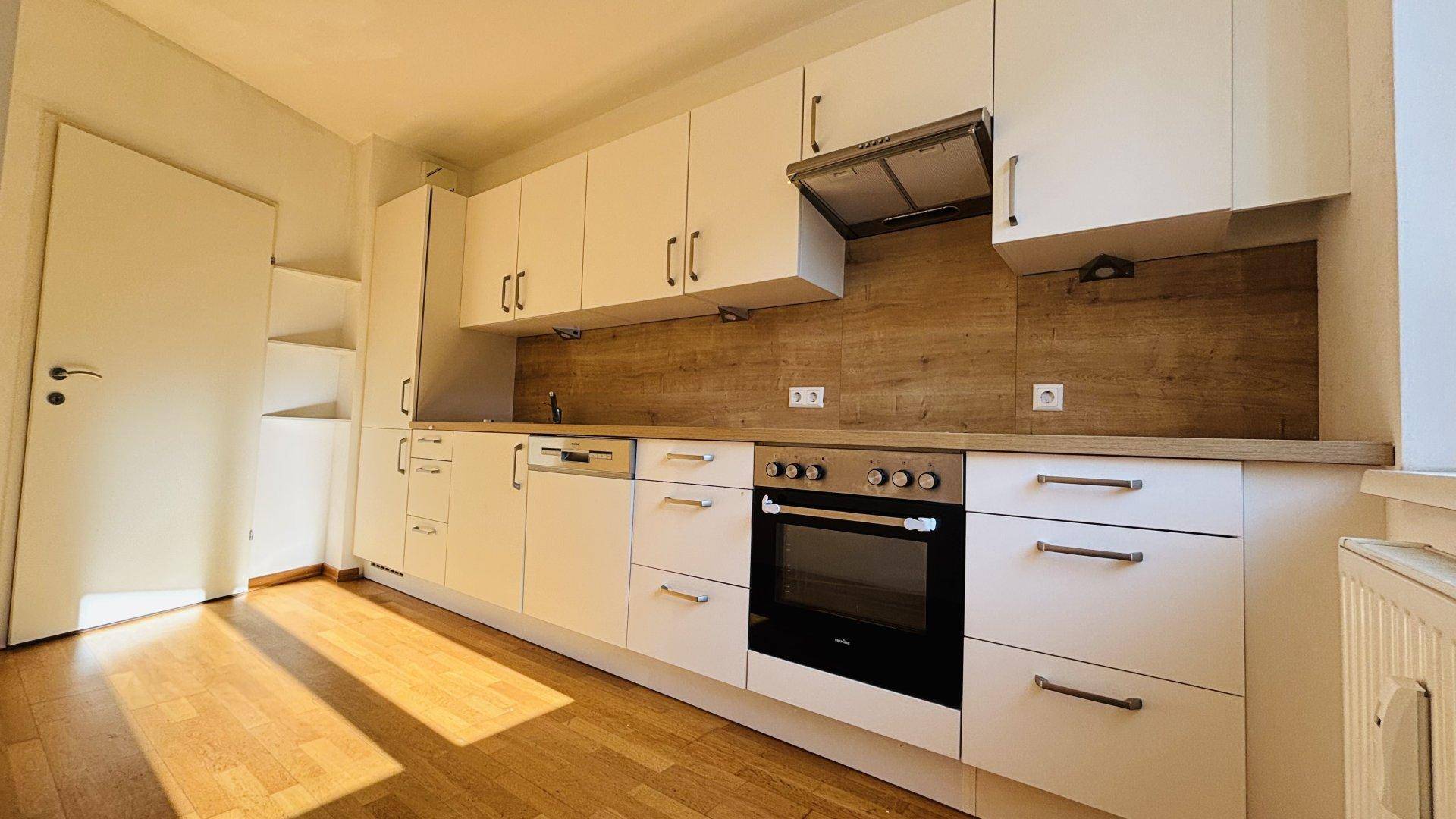 Moderne Einbauküche mit weißen Schränken, Holzoptik-Arbeitsplatte und integrierten Geräten.