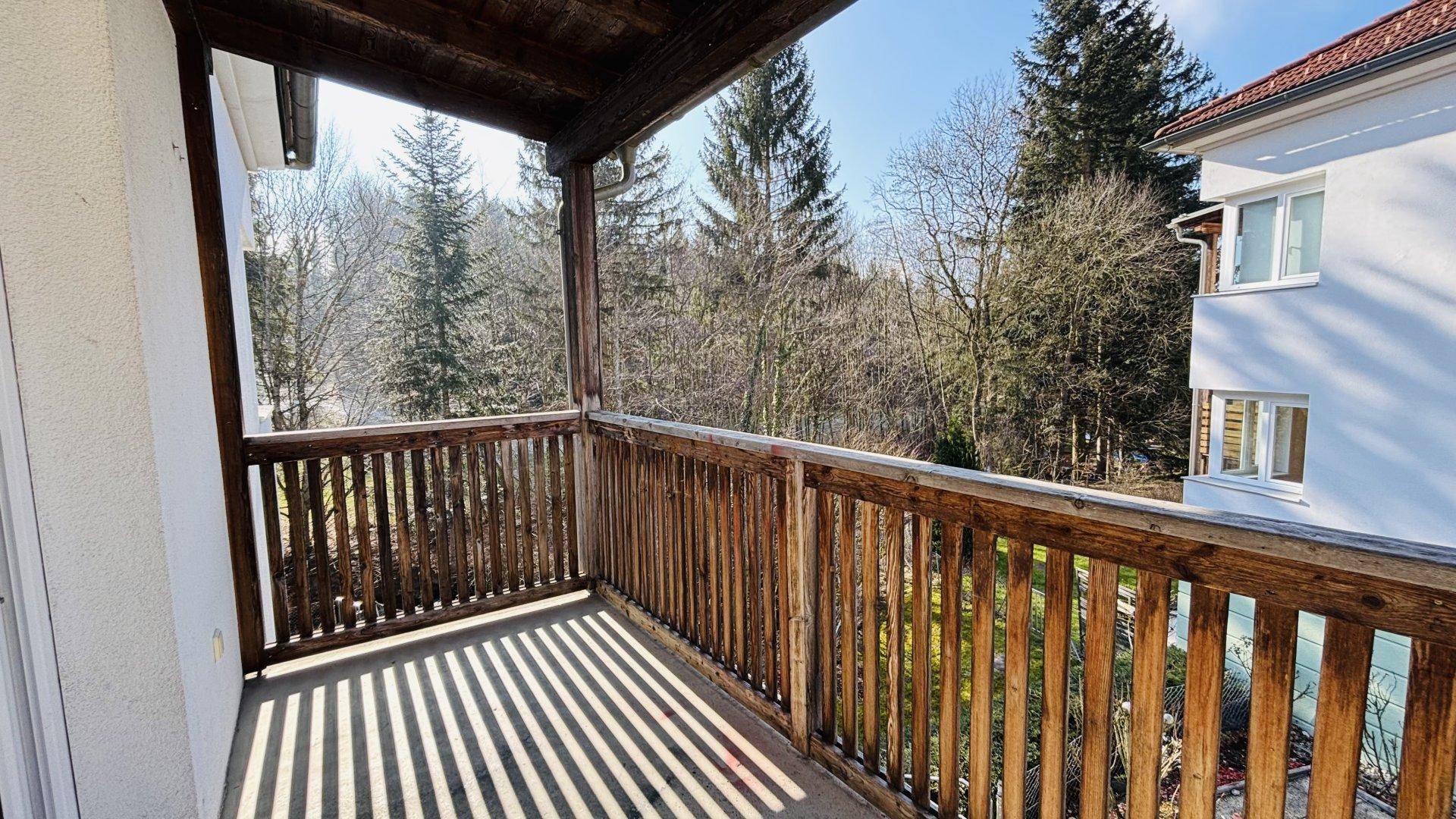 Überdachter Holzbalkon mit Blick ins Grüne und auf die umliegende Waldlandschaft.