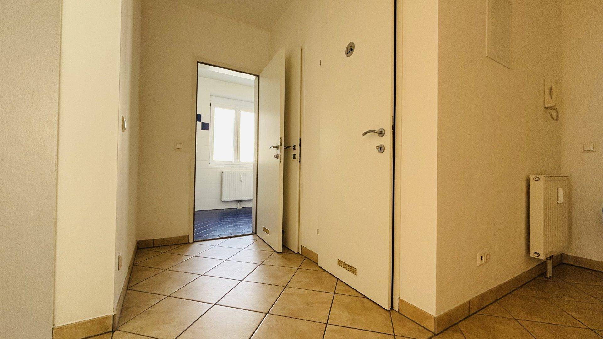 Eingangsbereich mit Fliesenboden, weißen Türen und einem Heizkörper an der Wand.