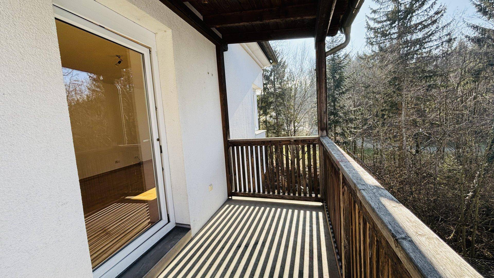 Geräumiger Holzbalkon mit schattenspendendem Dach und Zugang zum Innenbereich der Wohnung.