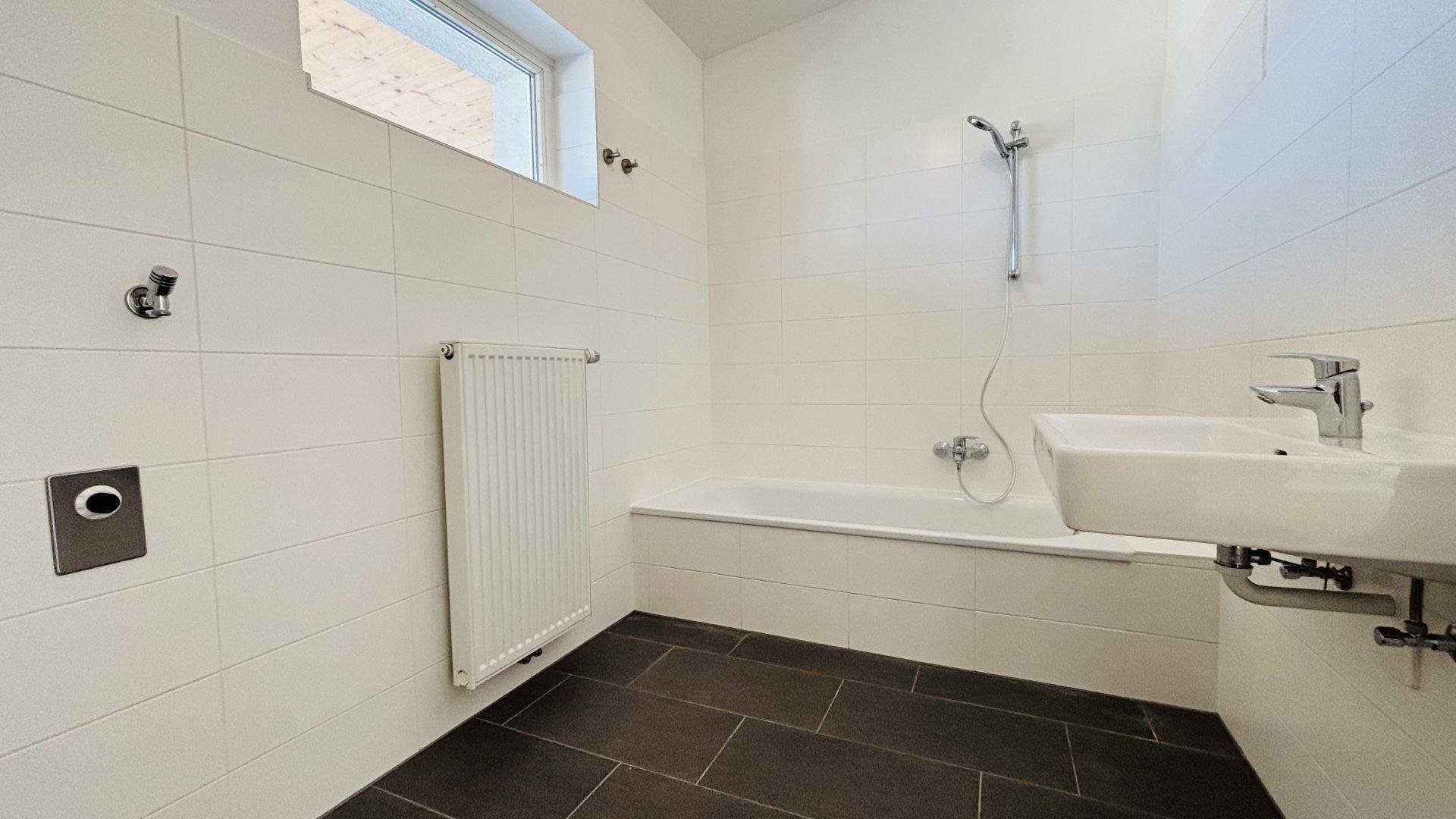 Modernes Badezimmer mit weißen Fliesen, Badewanne mit Duschfunktion und Waschbecken.