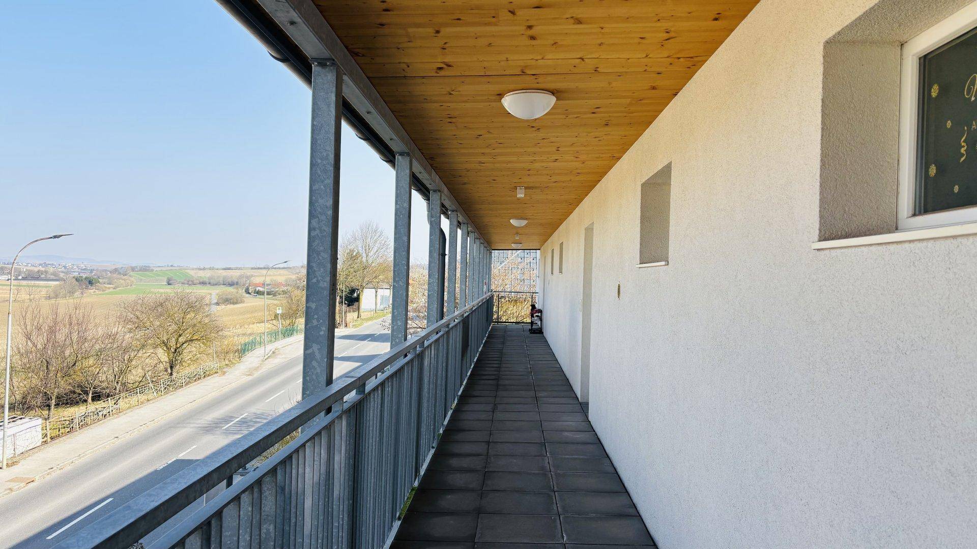 Langer überdachter Balkon mit Metallgeländer und weitem Blick über die Landschaft.