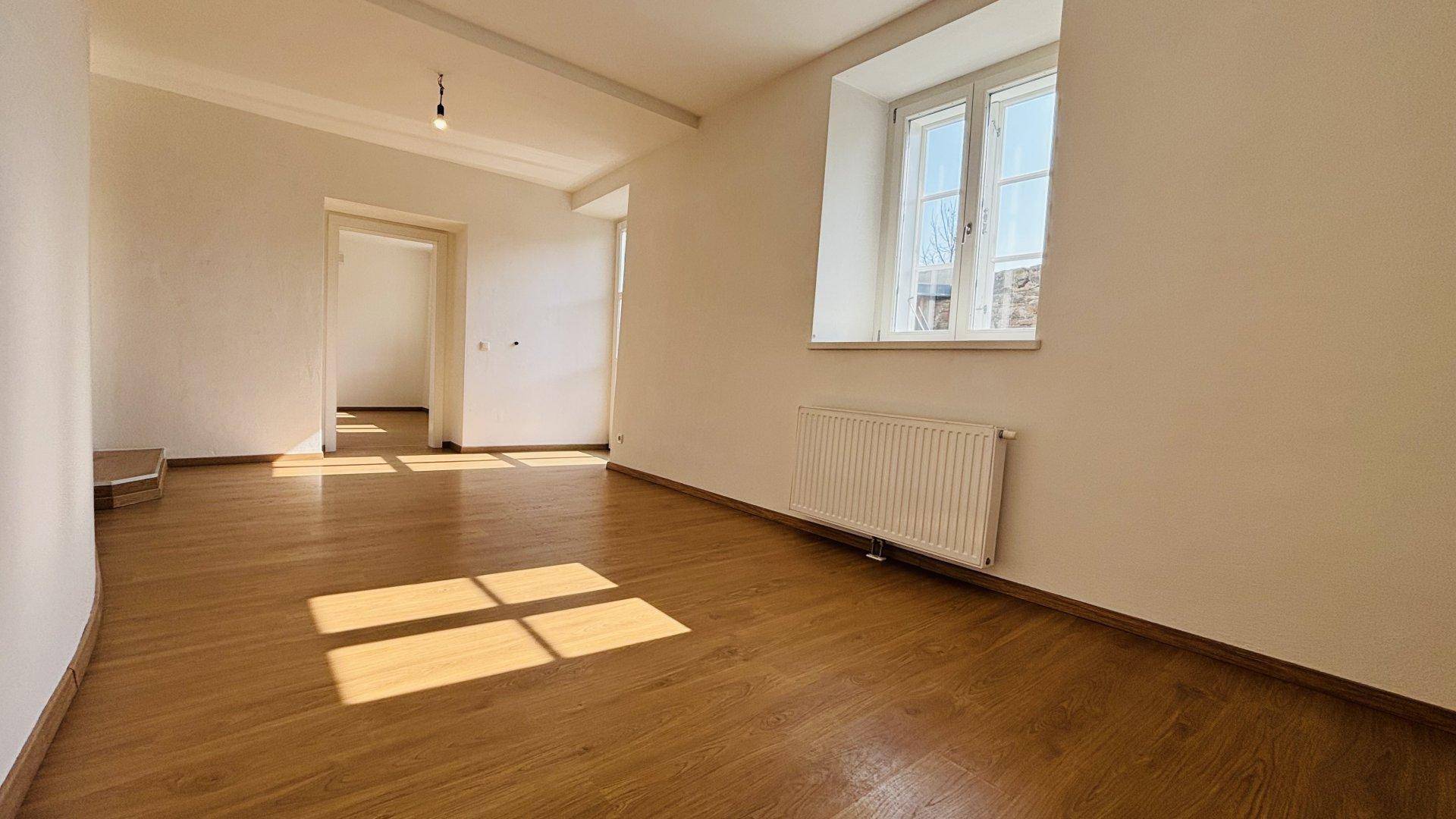 Heller Wohnraum mit Holzboden, weißen Wänden und viel natürlichem Licht durch das Fenster.