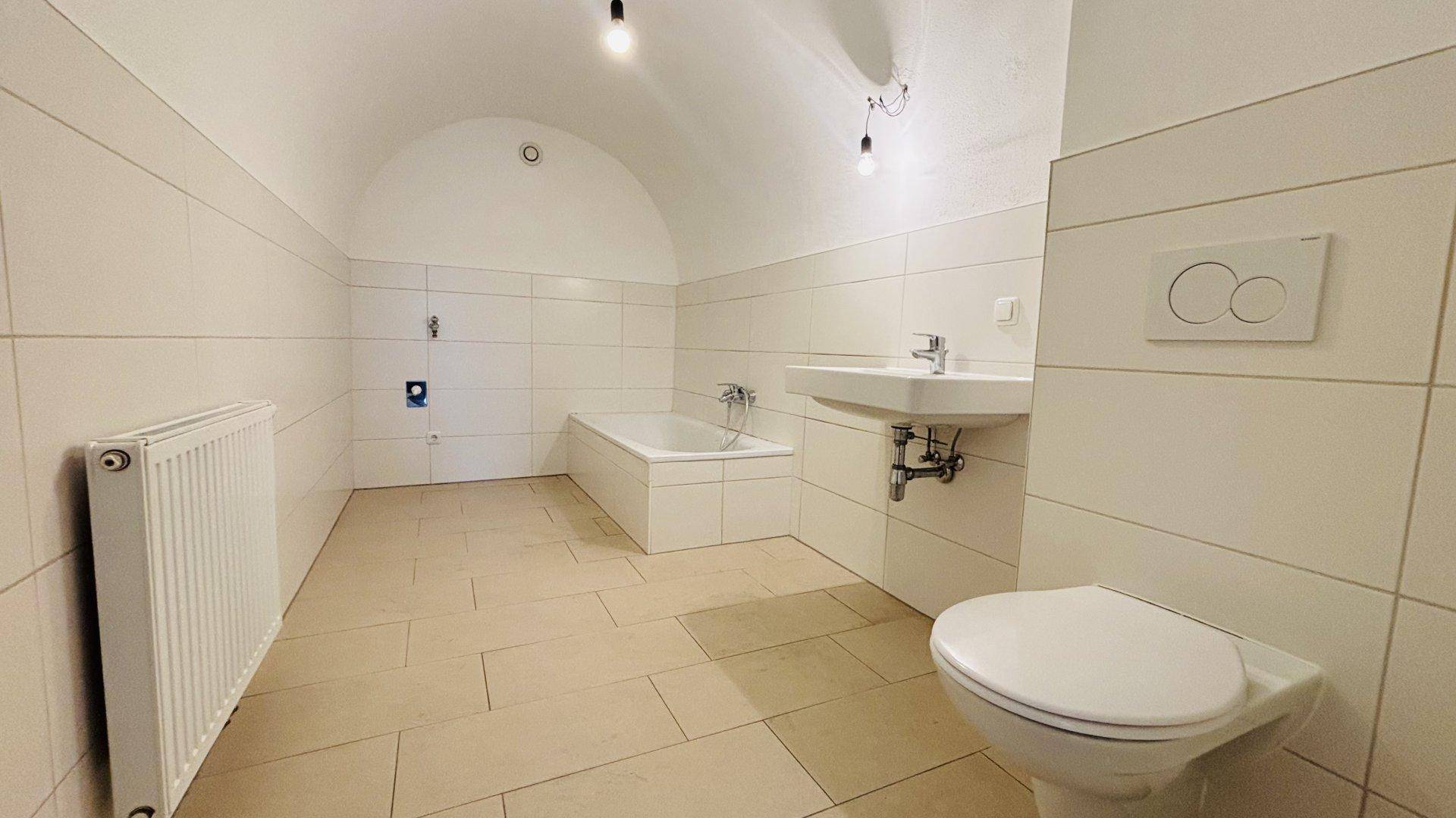 Modernes Badezimmer mit Fliesenboden, Badewanne, WC und Waschbecken unter einem Gewölbedach.