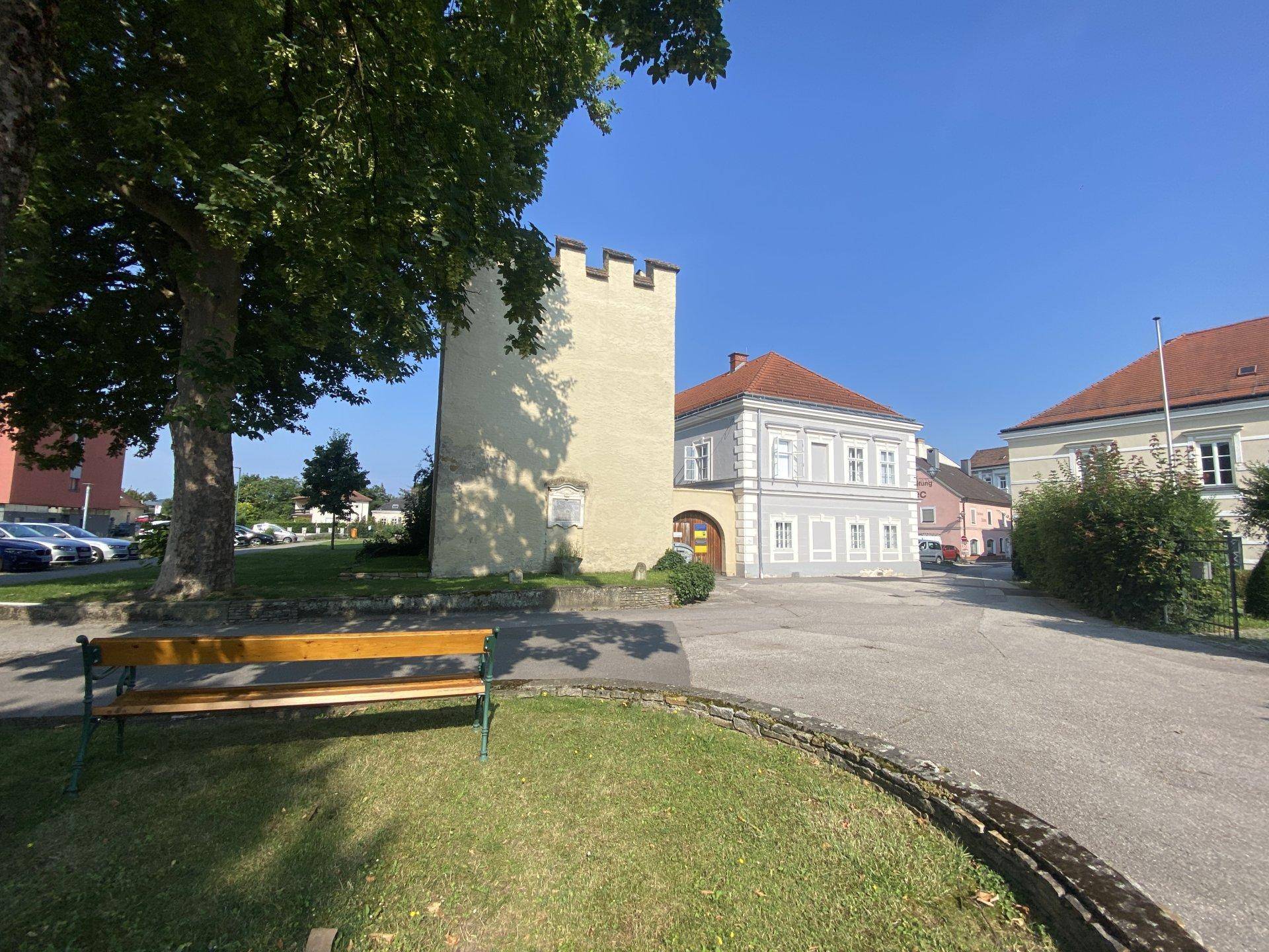 Historischer Turm und Gebäude in einer ländlichen Umgebung mit Sitzbank und Baum.