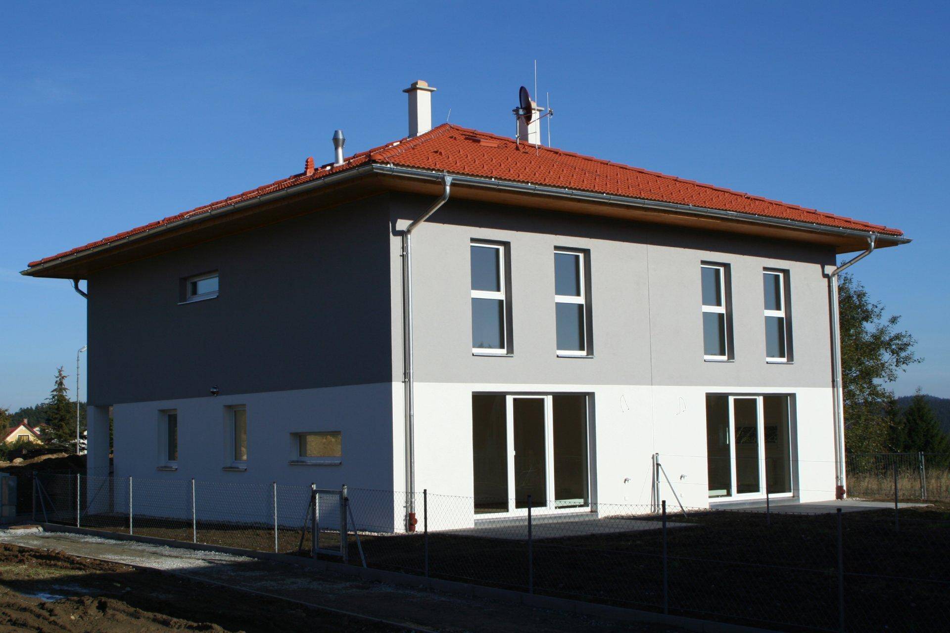 Rückansicht des Neubaus mit rotem Ziegeldach und großen Fenstern, umgeben von ländlicher Natur.