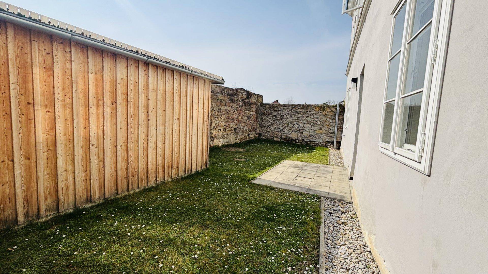Ruhiger Gartenbereich mit Holzschuppen und Kiesstreifen entlang der Hauswand, sonnig gelegen.