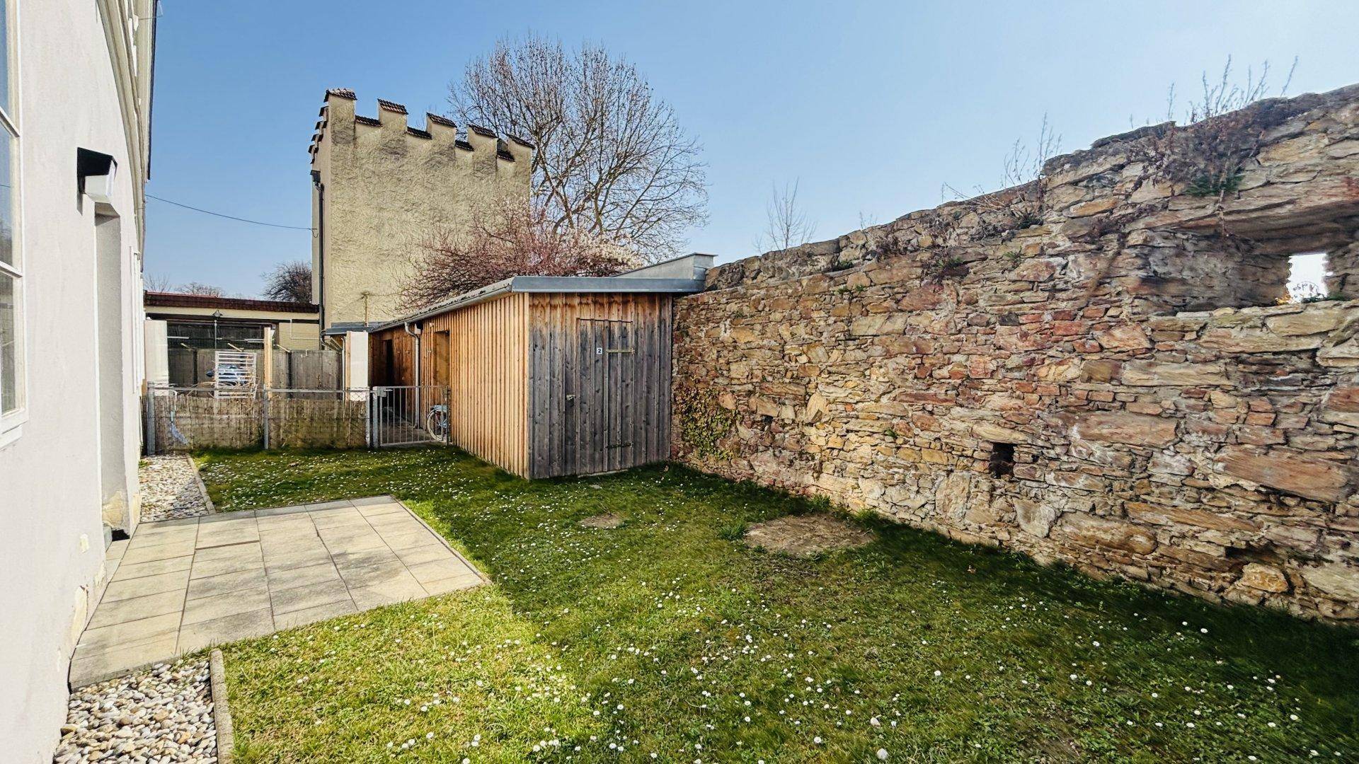 Gepflegter Garten mit Holzschuppen und historischer Steinmauer, bietet viel Privatsphäre.