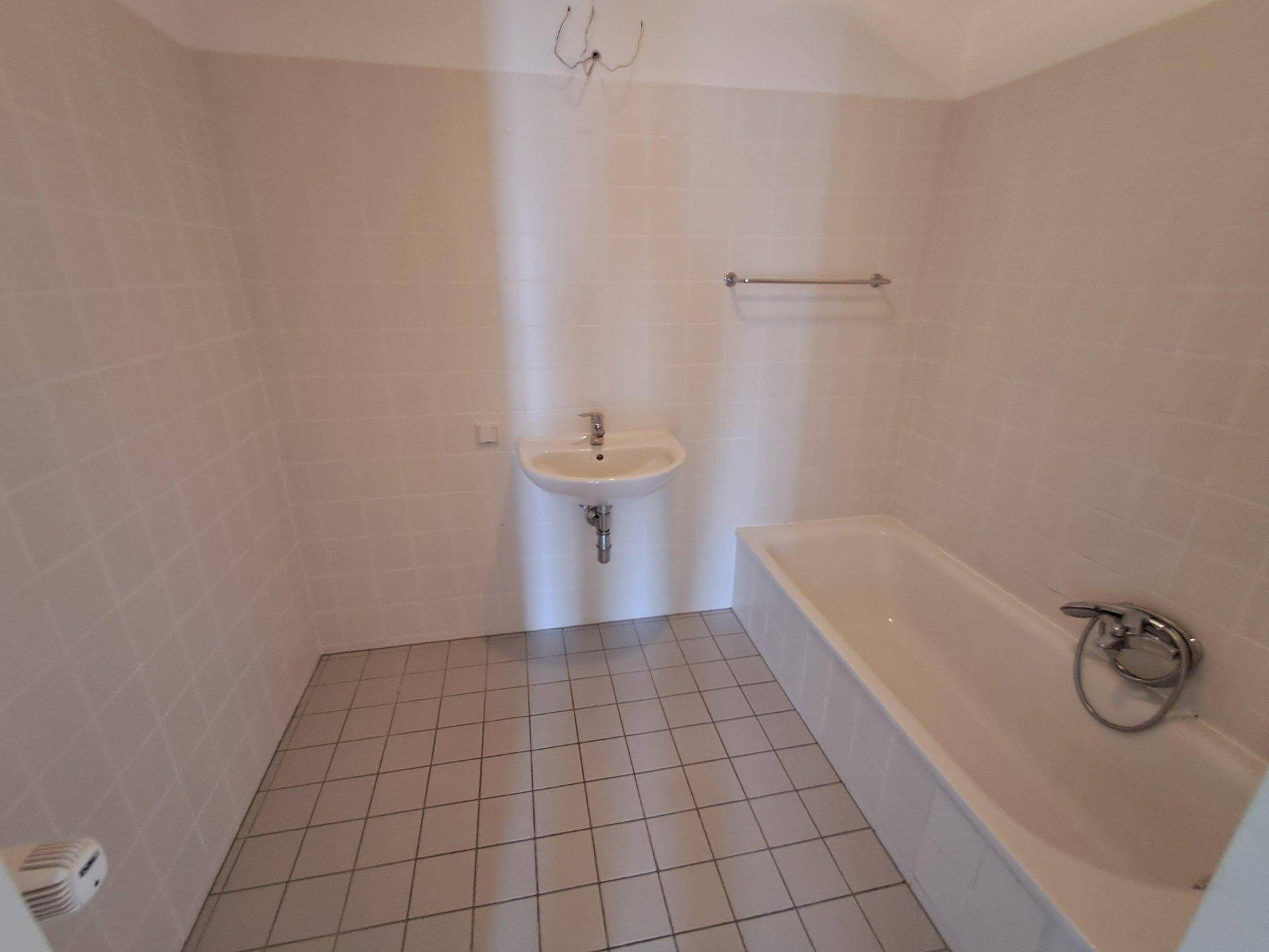 Badezimmer mit Fliesenboden, Badewanne und Waschbecken, bereit zur individuellen Gestaltung.