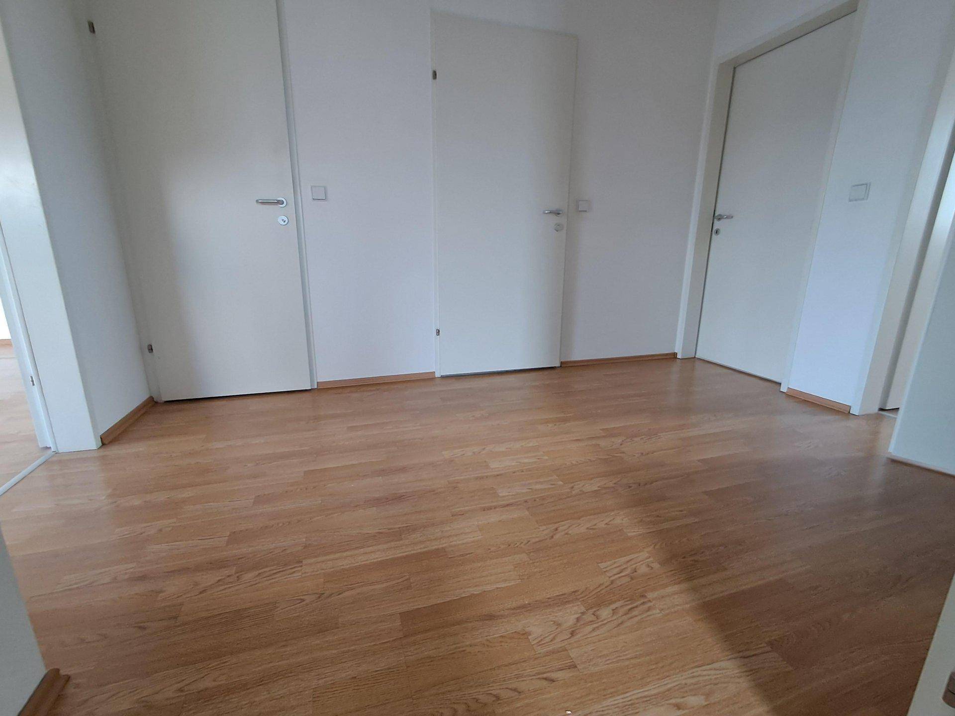 Leerer Raum mit hellem Holzboden und weißen Türen, bereit zur individuellen Gestaltung und Nutzung.