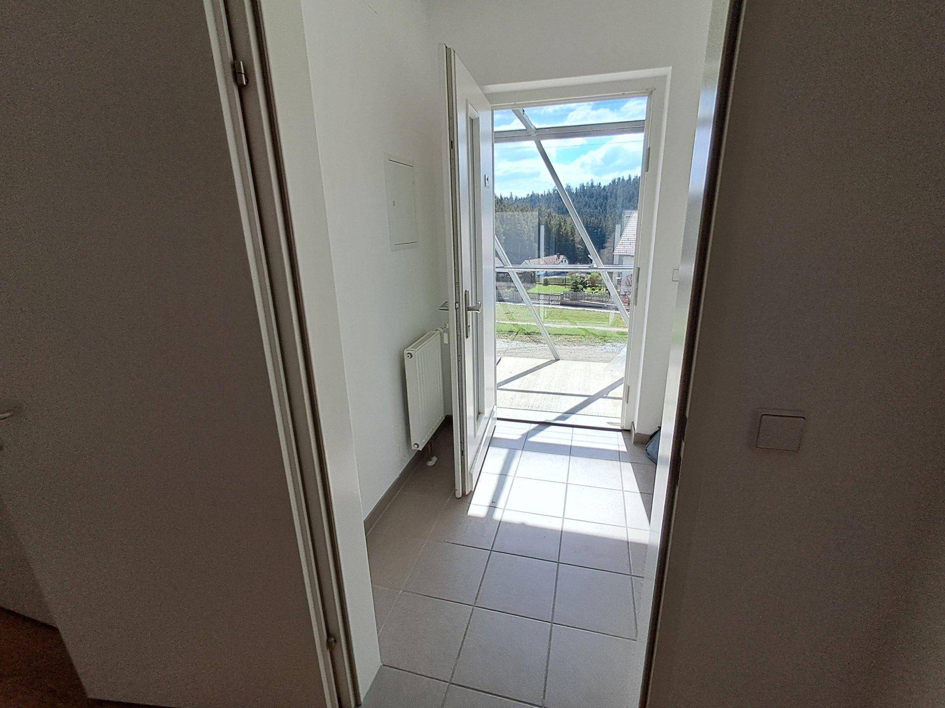 Heller Flur mit Fliesenboden und Zugang zu einem Balkon mit weitem Blick ins Grüne.