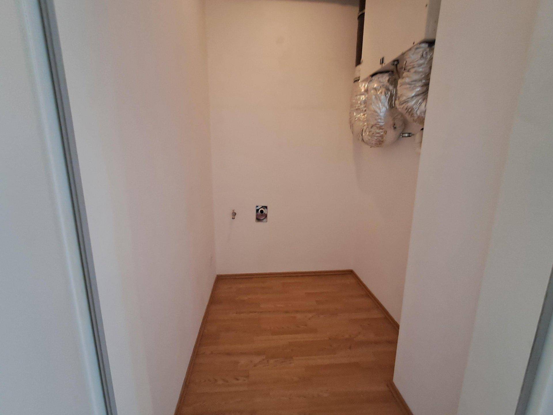 Kleiner Hauswirtschaftsraum mit Anschlüssen und Holzboden, ideal für Waschmaschine und Trockner.