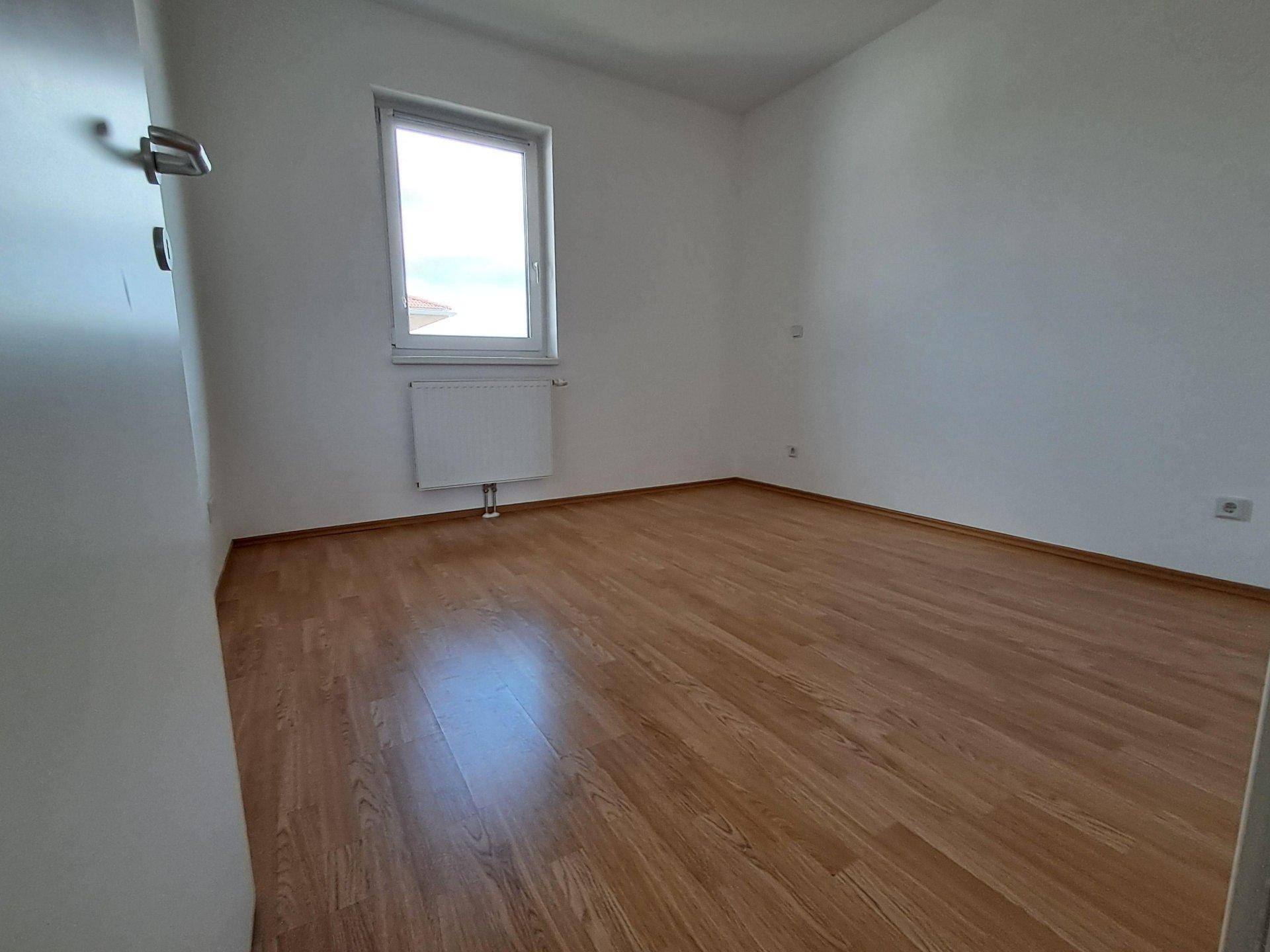 Helles Schlafzimmer mit Holzboden und einem Fenster, das viel Tageslicht hereinlässt.