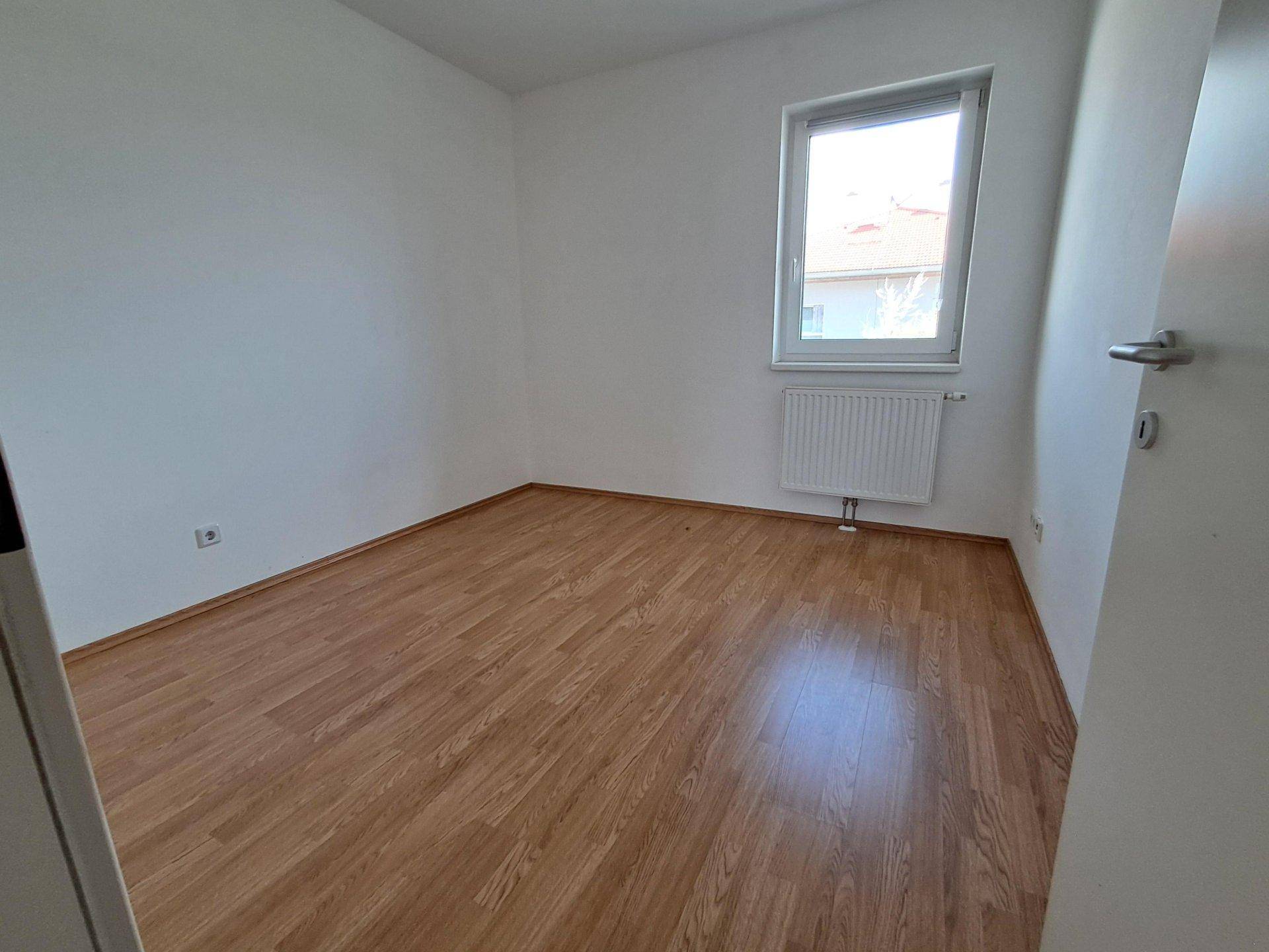 Gemütliches Schlafzimmer mit Holzboden und einem Fenster, das eine ruhige Atmosphäre schafft.