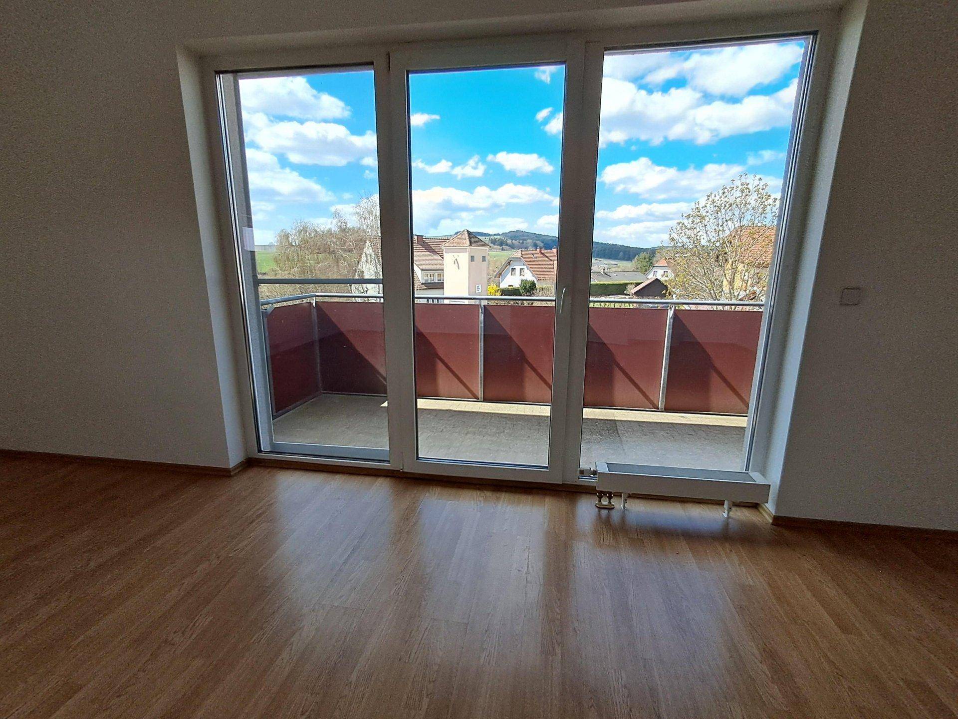 Heller Raum mit Holzboden und breiter Balkontür, die einen weiten Blick auf die Umgebung bietet.