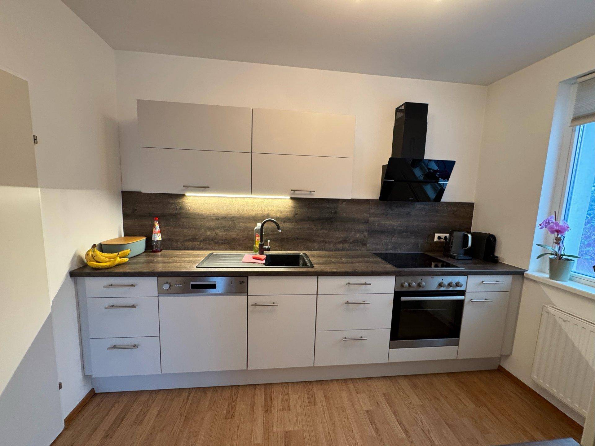 Moderne Küche mit hellen Schränken, dunkler Arbeitsplatte und integrierten Geräten.