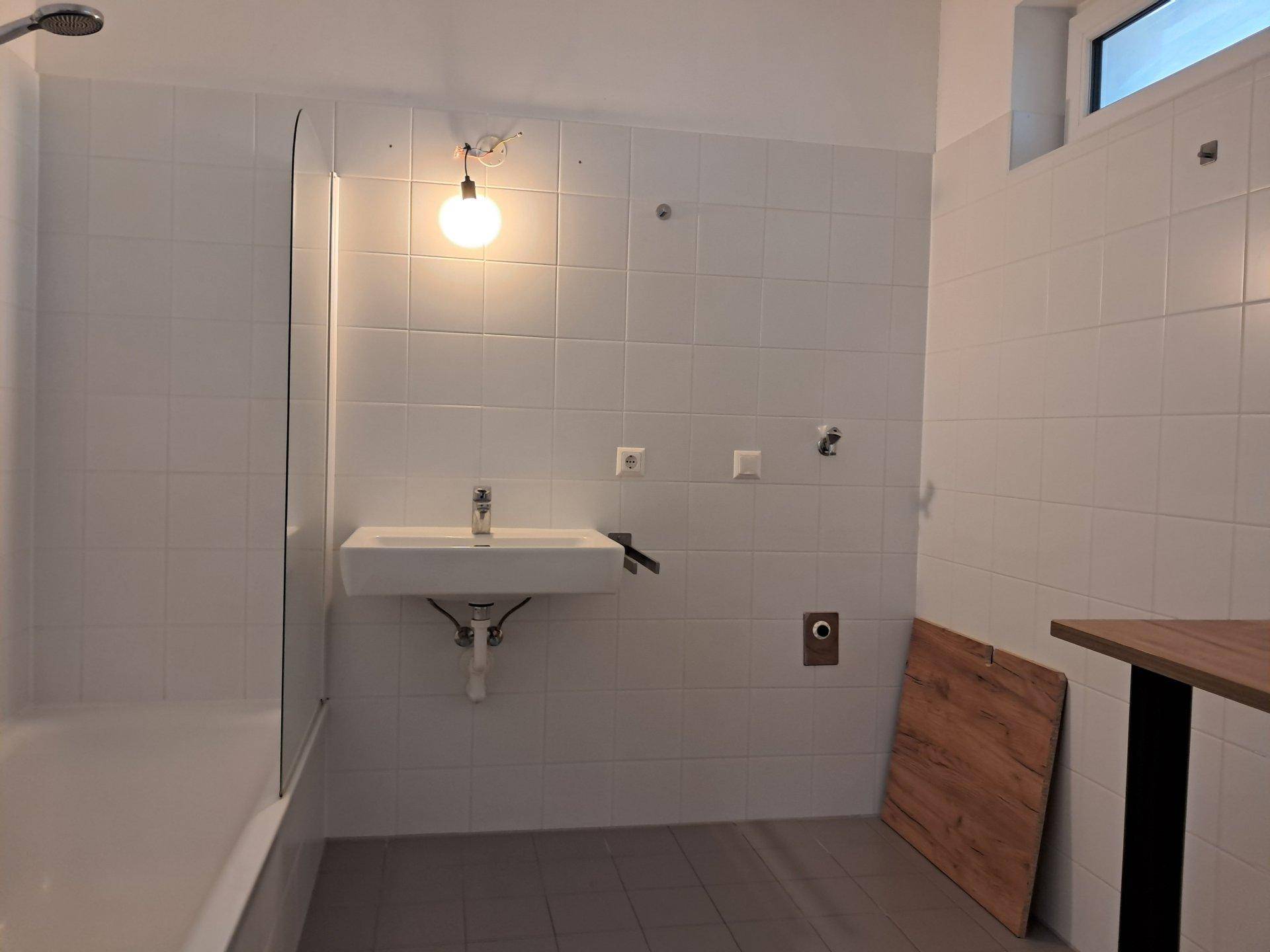 Helles Badezimmer mit Waschbecken, Dusch-Badewannenbereich und Fenster.