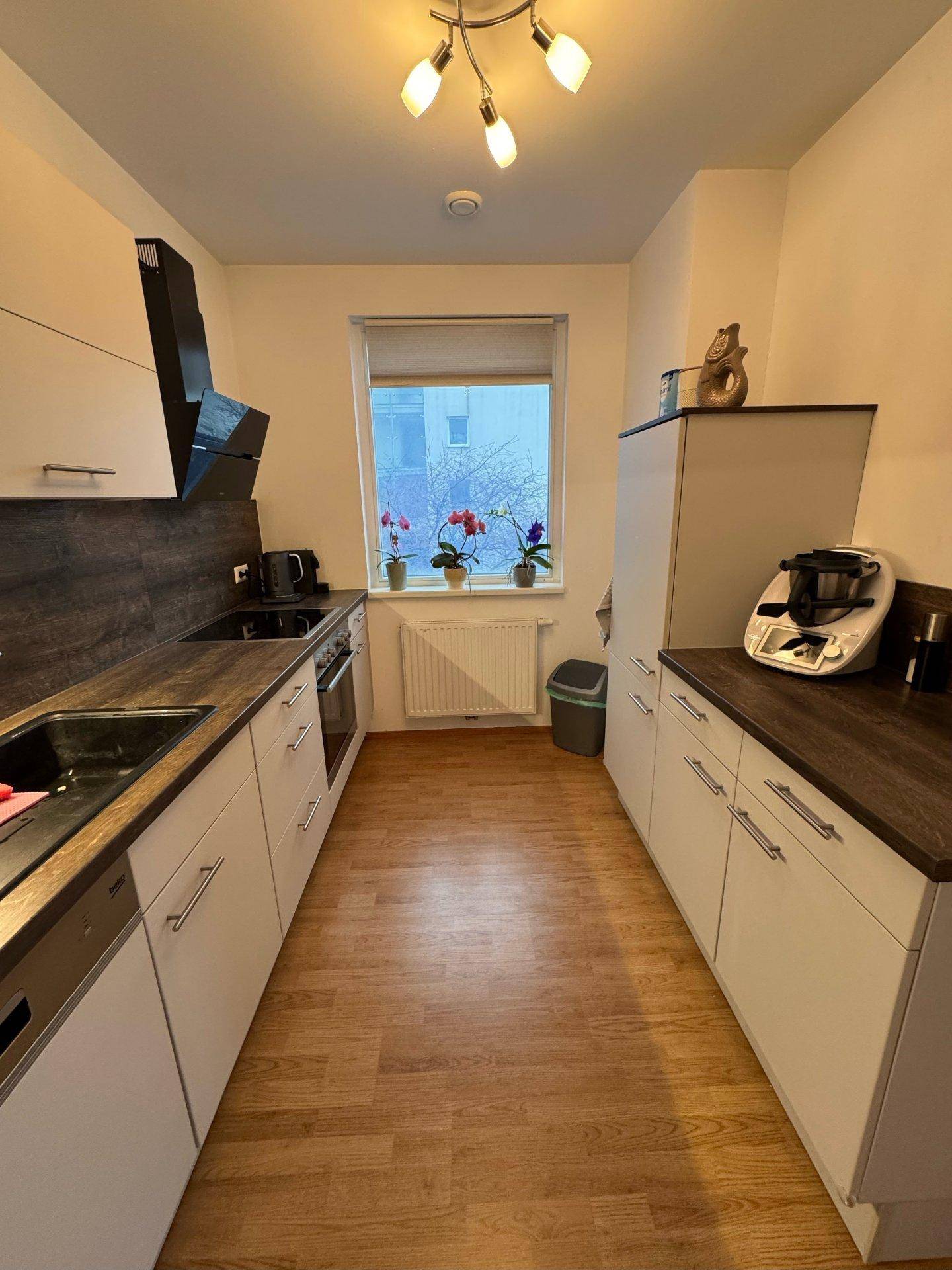 Helle Küchenzeile mit Fenster, Laminatboden und modernen Einbauschränken.