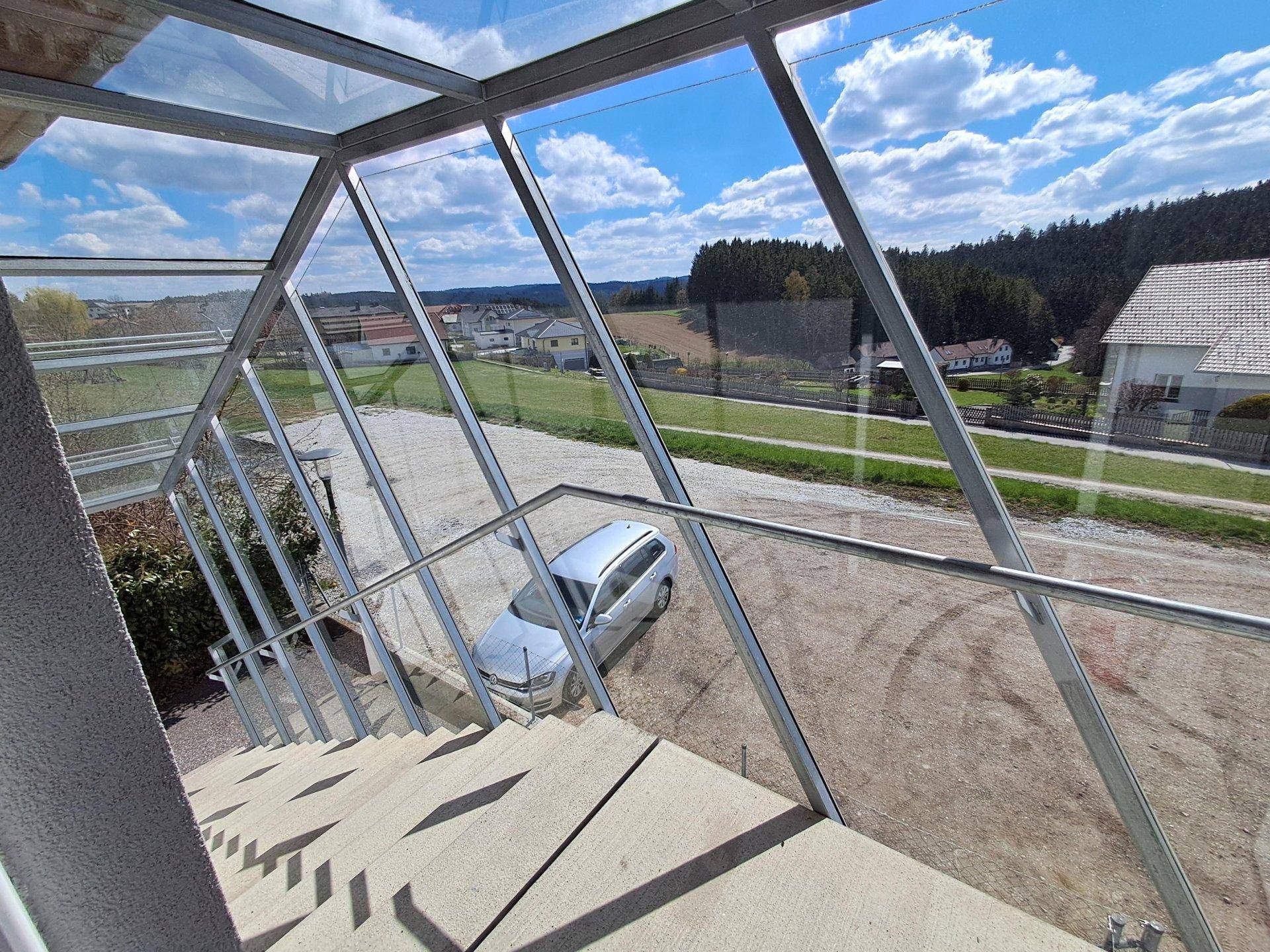 Verglaste Außentreppe mit Metallgeländer, die einen Panoramablick auf die Umgebung bietet.