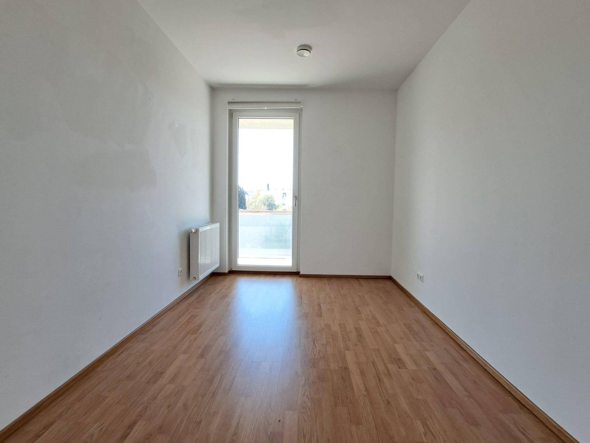 Leeres Zimmer mit Laminatboden und hellem Zugang zum Außenbereich.