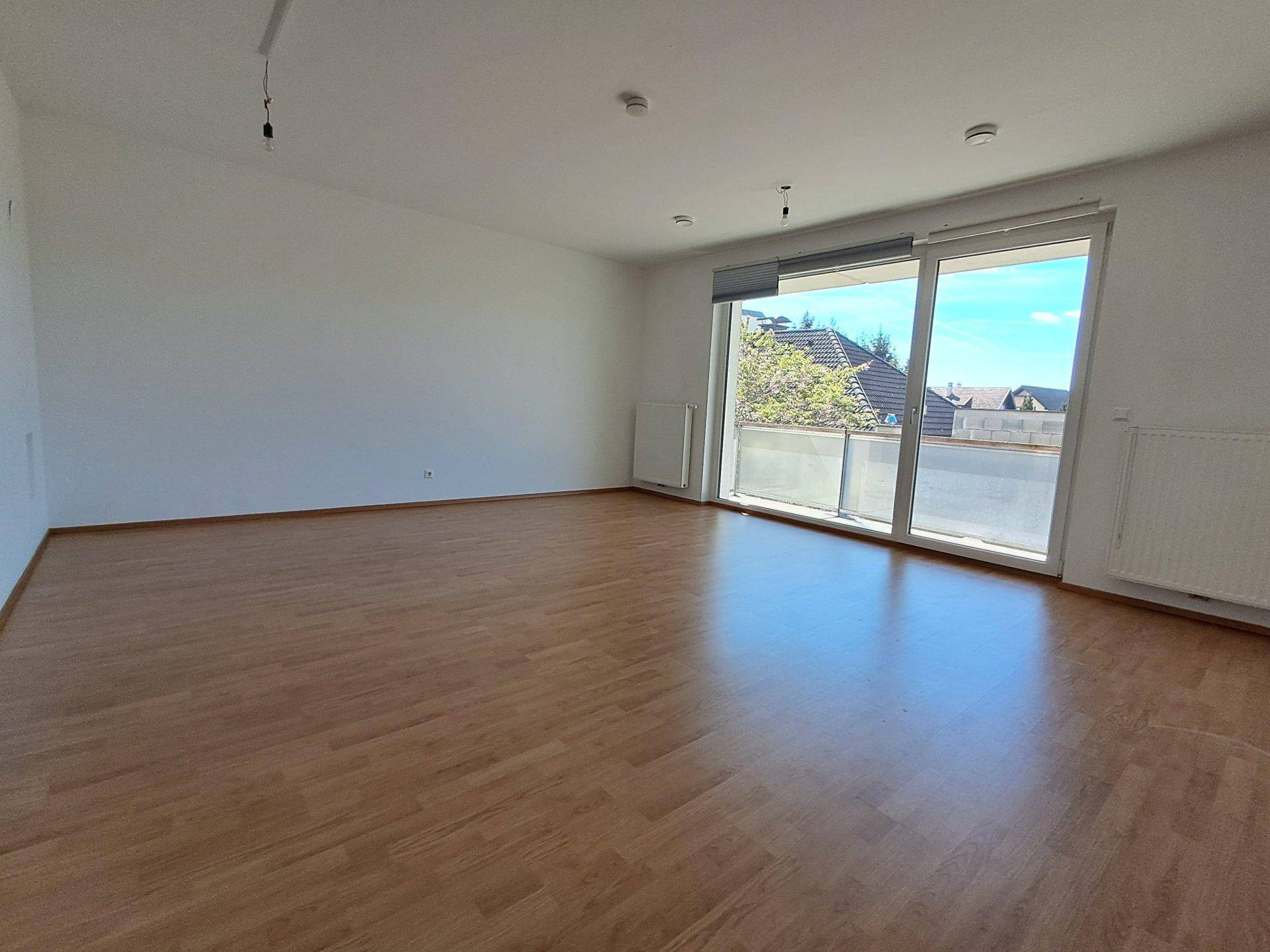 Geräumiges Wohnzimmer mit Laminatboden und großer Schiebetür zum Balkon.