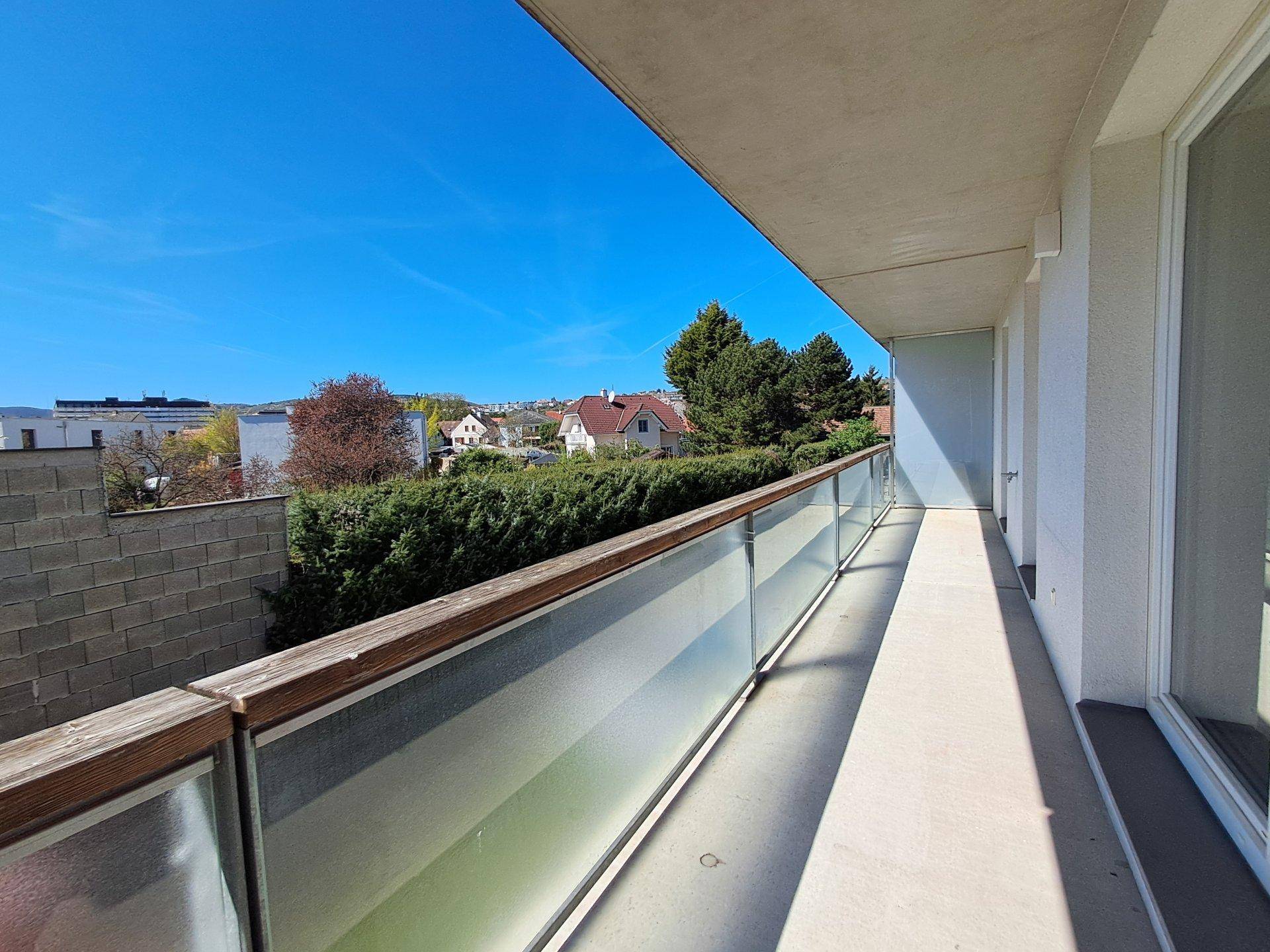 Langer Balkon mit Glasgeländer und Blick auf die umliegende Wohngegend.