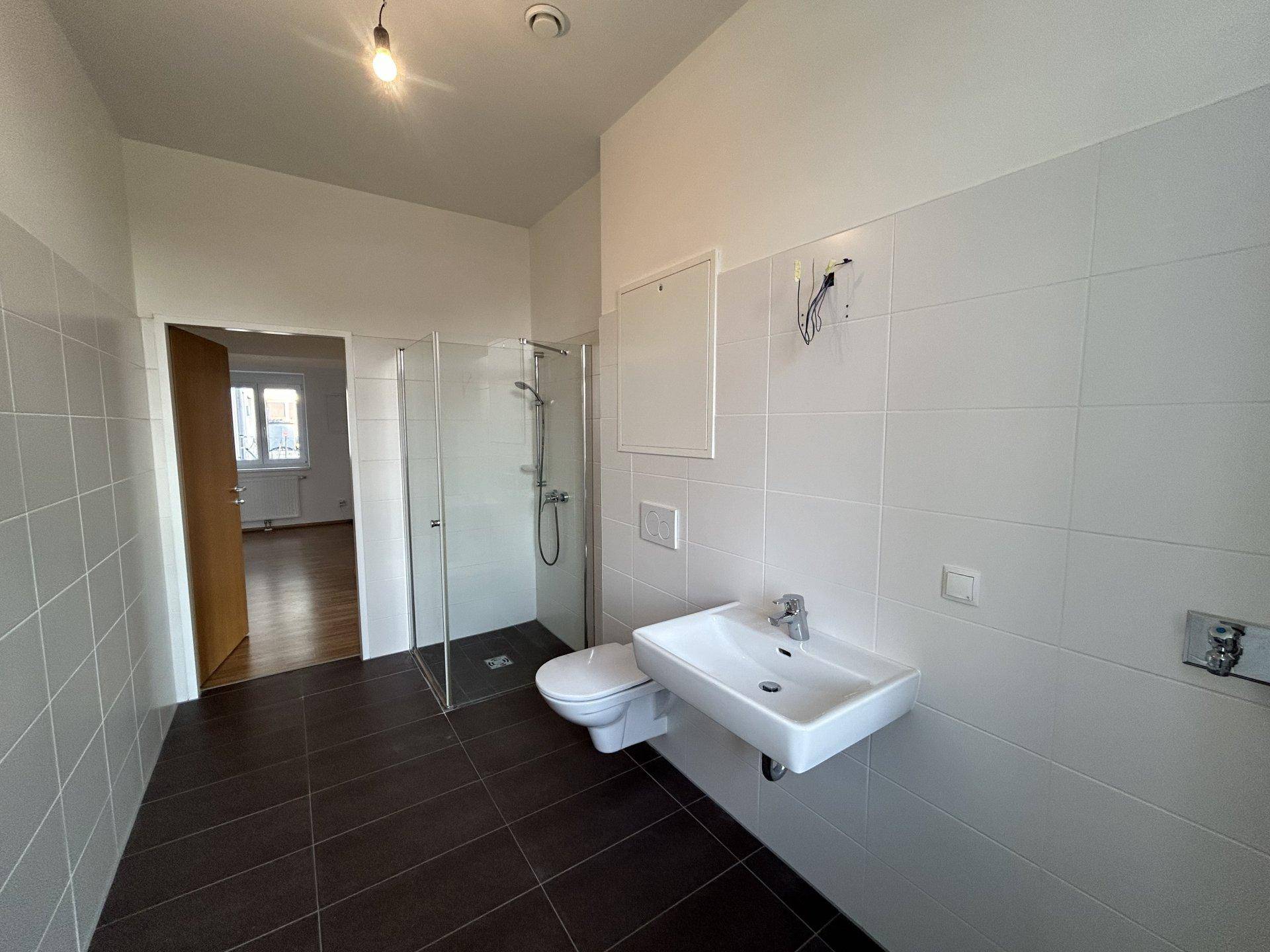 Geräumiges Badezimmer mit Duschkabine, wandhängendem WC und Waschbecken.