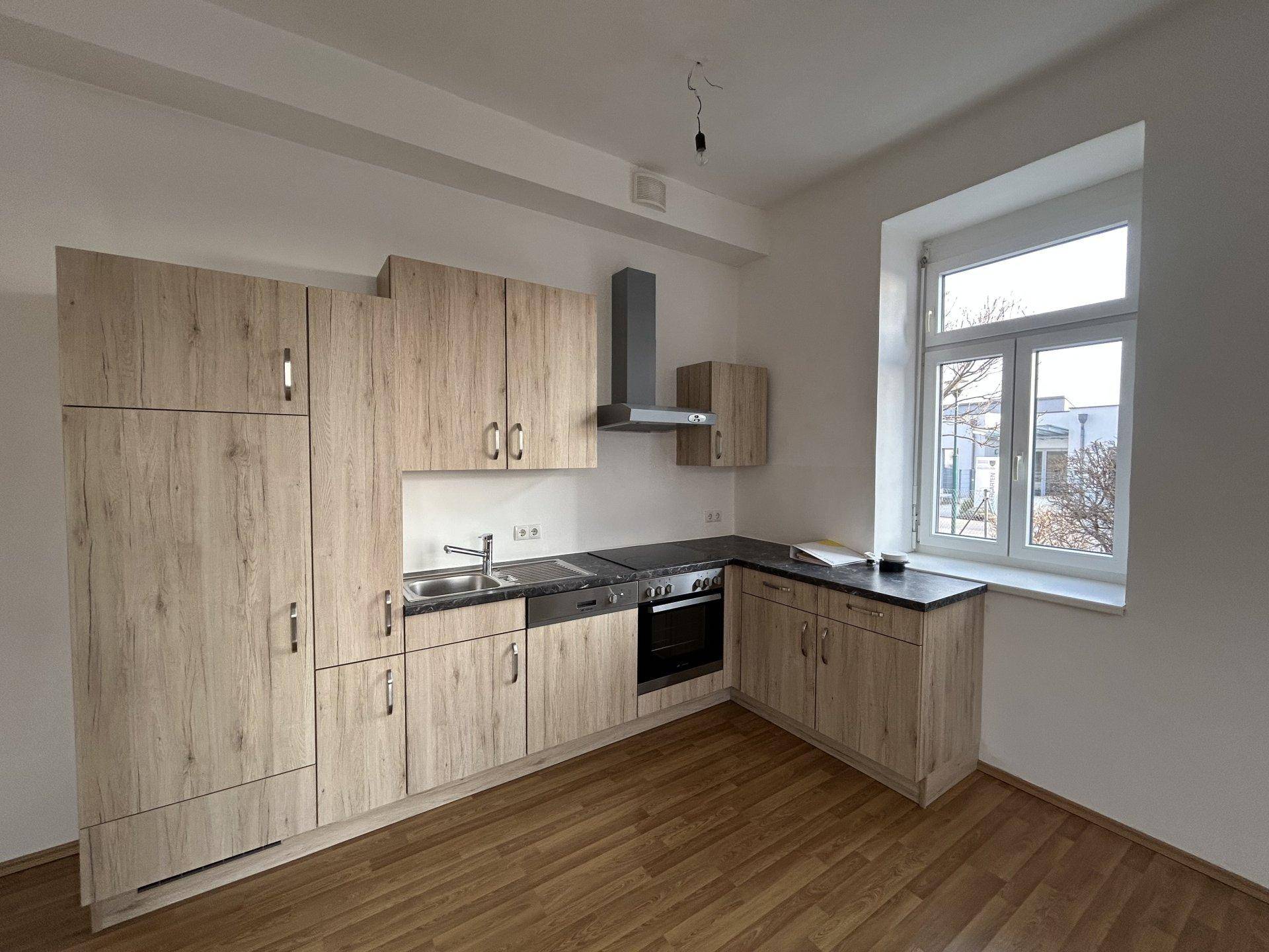 Neue Einbauküche in Holzoptik mit modernen Geräten und einem Fenster.