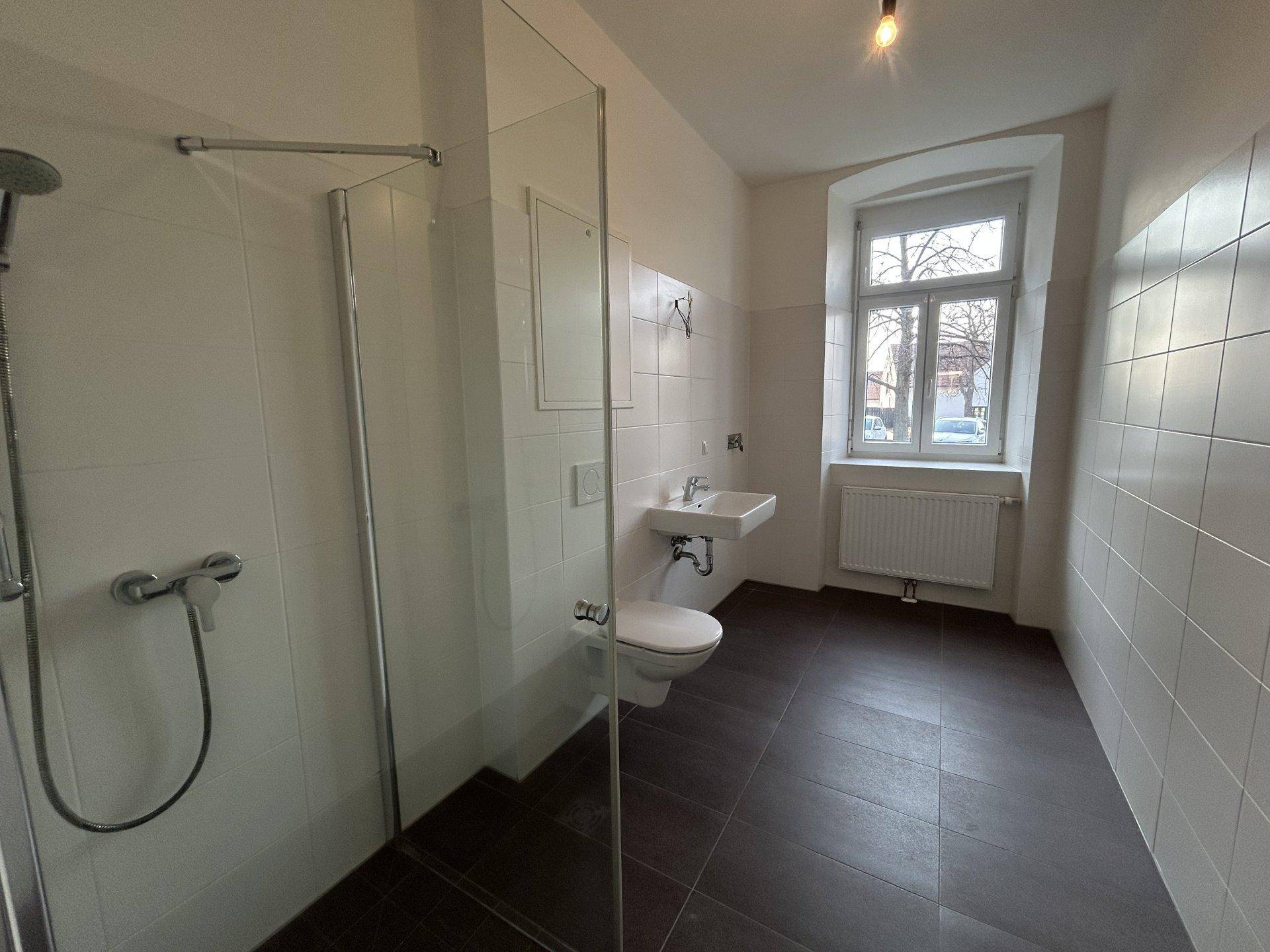 Modernes Badezimmer mit Dusche, WC, Waschbecken und einem Fenster für Tageslicht.