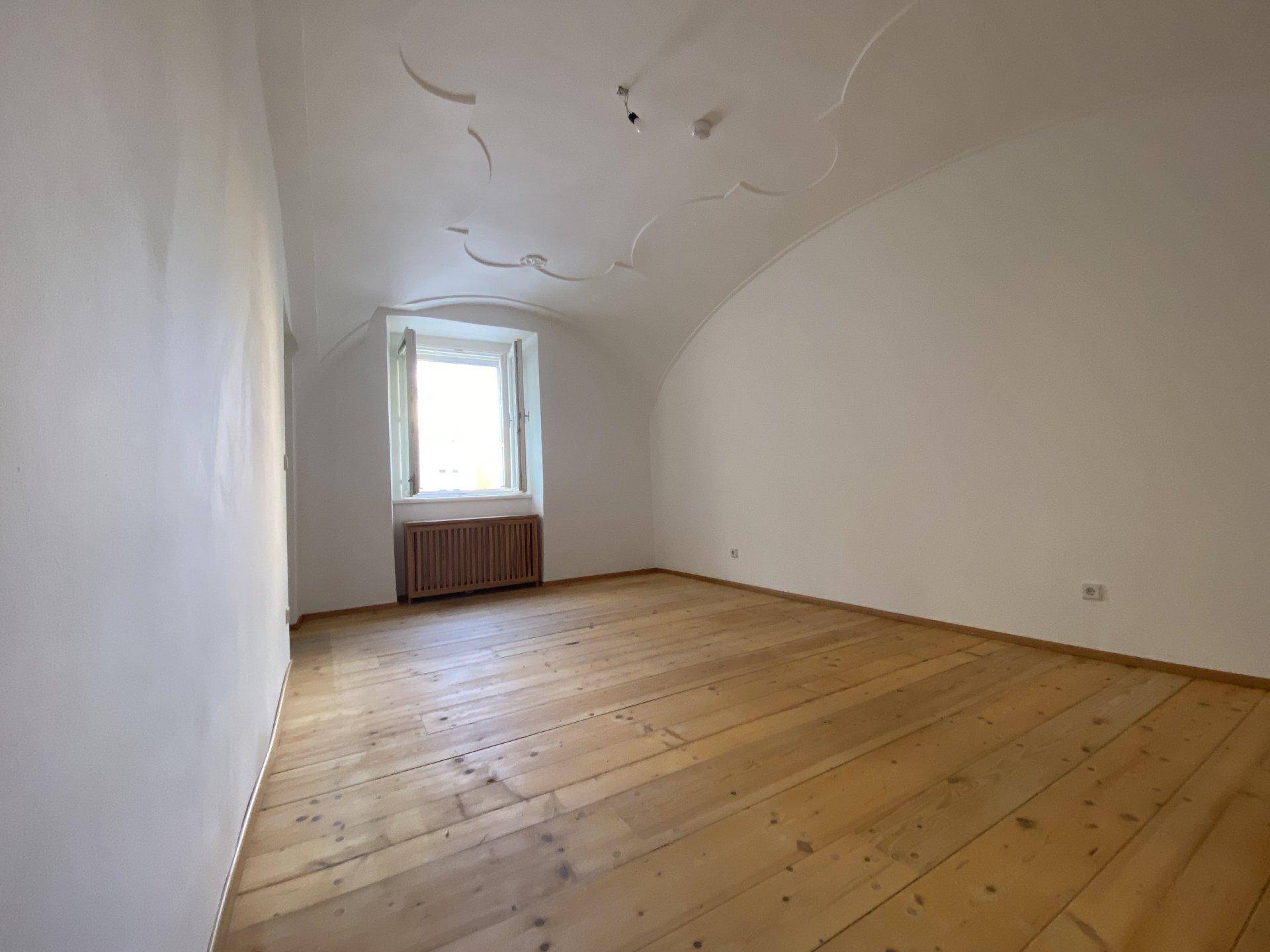 Gemütliches Schlafzimmer mit breiten Holzplanken, einem Fenster und einer gewölbten Decke.