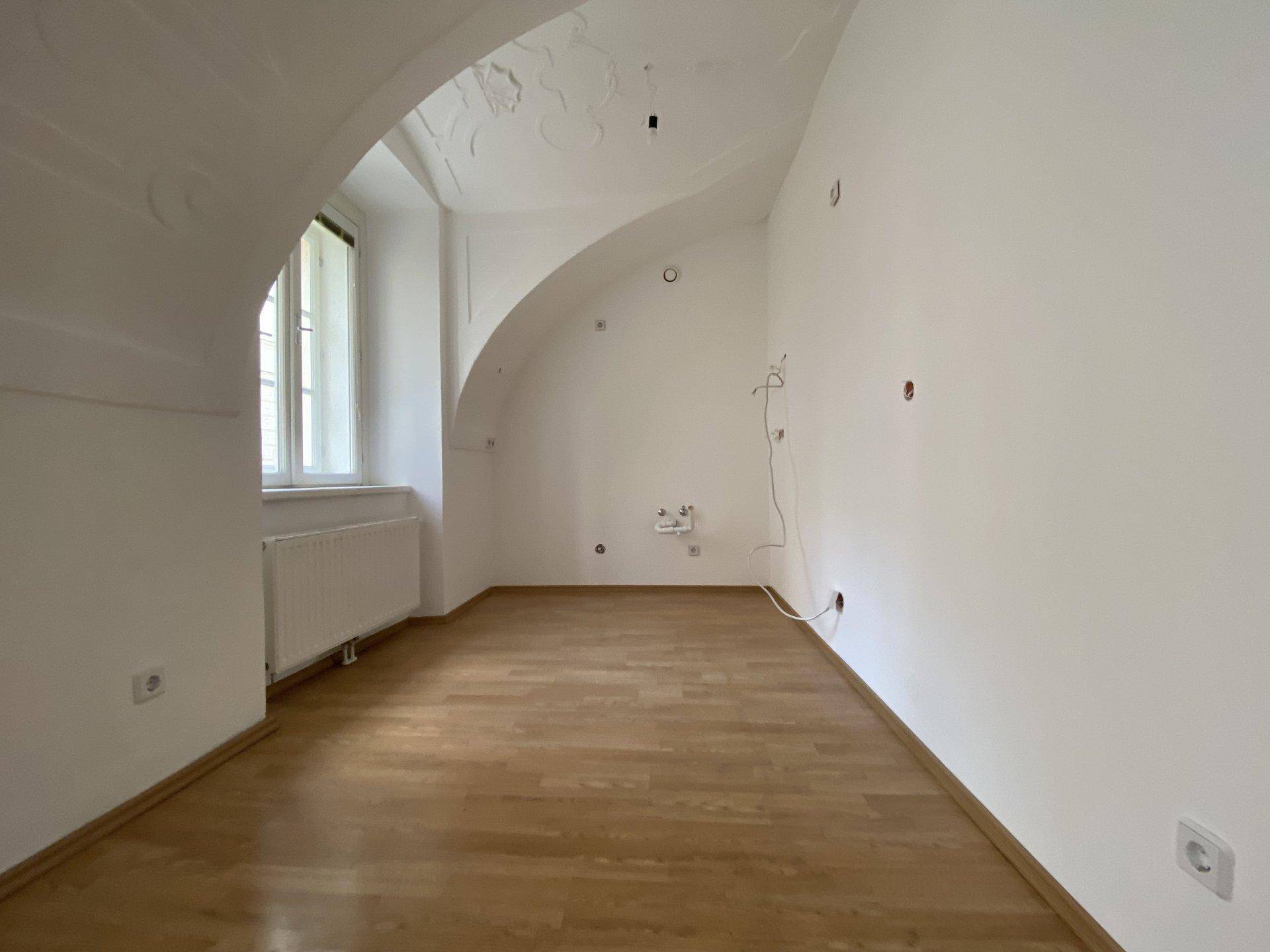 Heller Raum mit Holzboden, gewölbter Decke und einem Fenster, bereit für die individuelle Gestaltung.