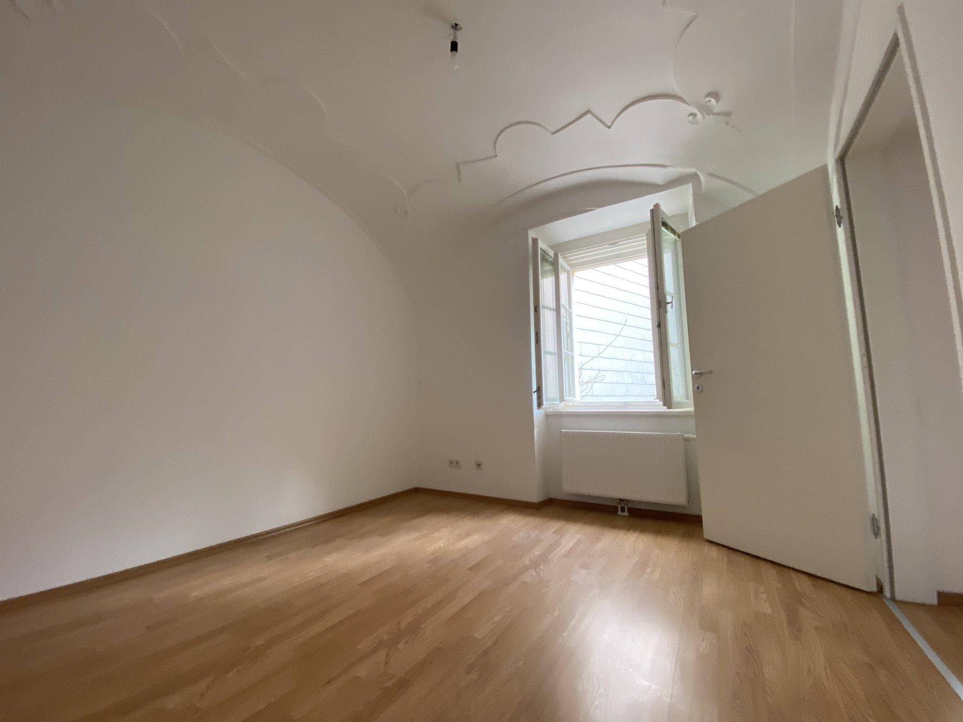 Helles Schlafzimmer mit Holzboden, offenem Fenster und einer gewölbten Decke, bereit zum Einzug.