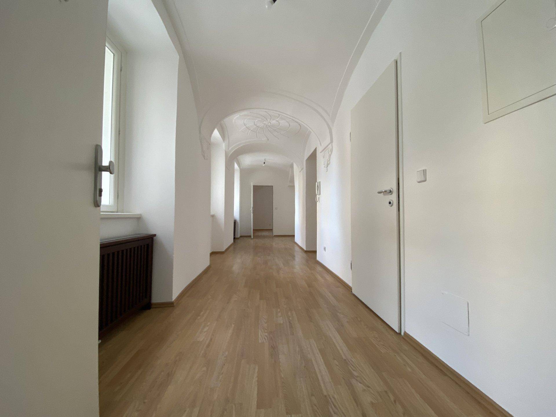 Langer, heller Flur mit Holzboden, gewölbter Decke und mehreren Türen zu angrenzenden Räumen.