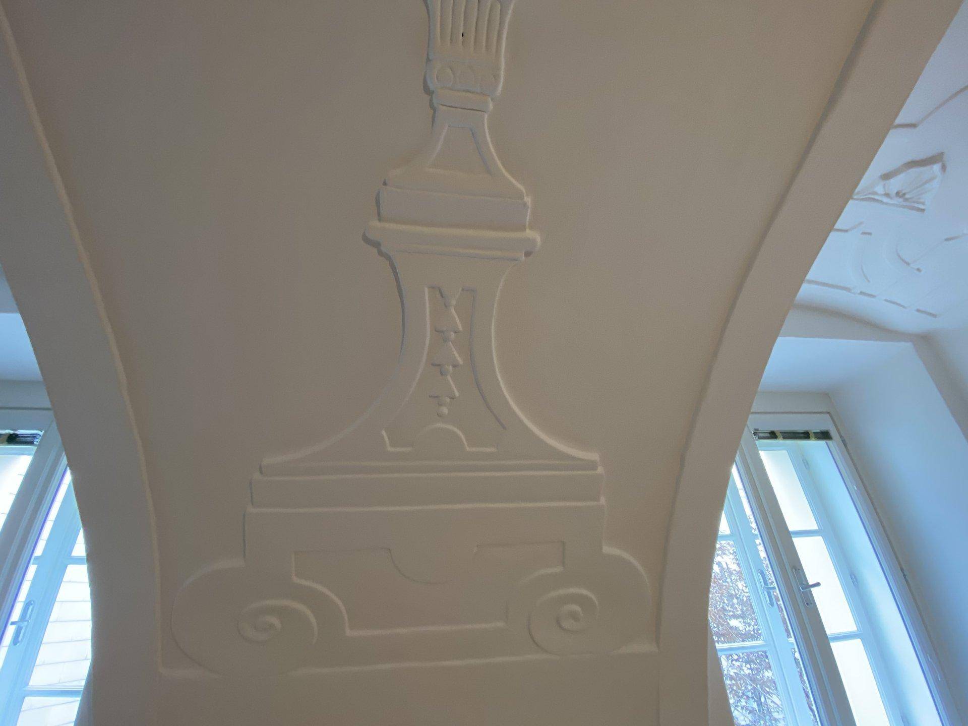 Weiße Decke mit imposanter Stuckverzierung und hohen Fenstern, die viel natürliches Licht hereinlassen.