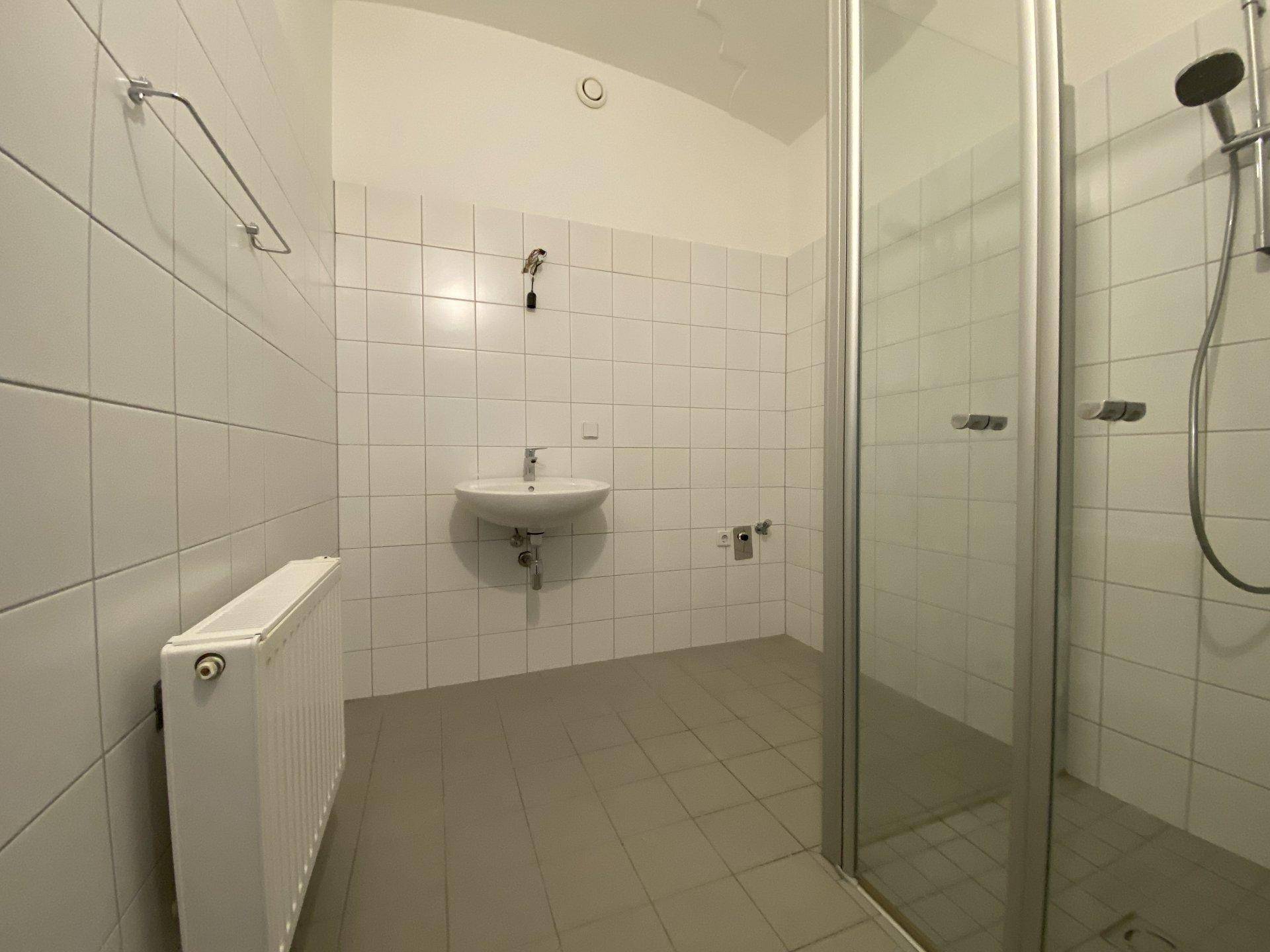 Modernes Badezimmer mit Duschkabine, Waschbecken und hellen Fliesen an Wänden und Boden.