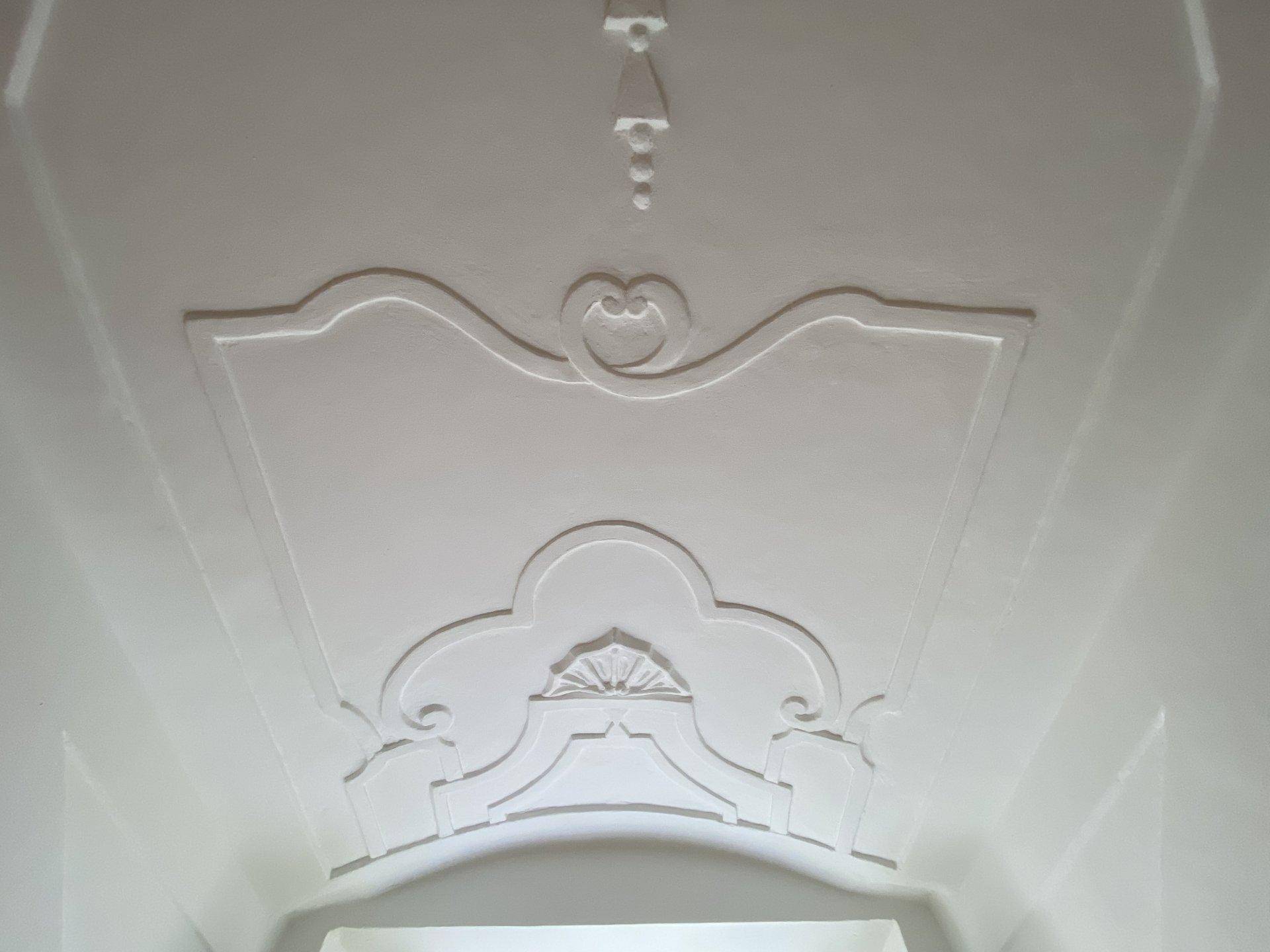 Weiße Decke mit aufwendiger Stuckverzierung und klassischen Ornamenten, die Eleganz verleiht.