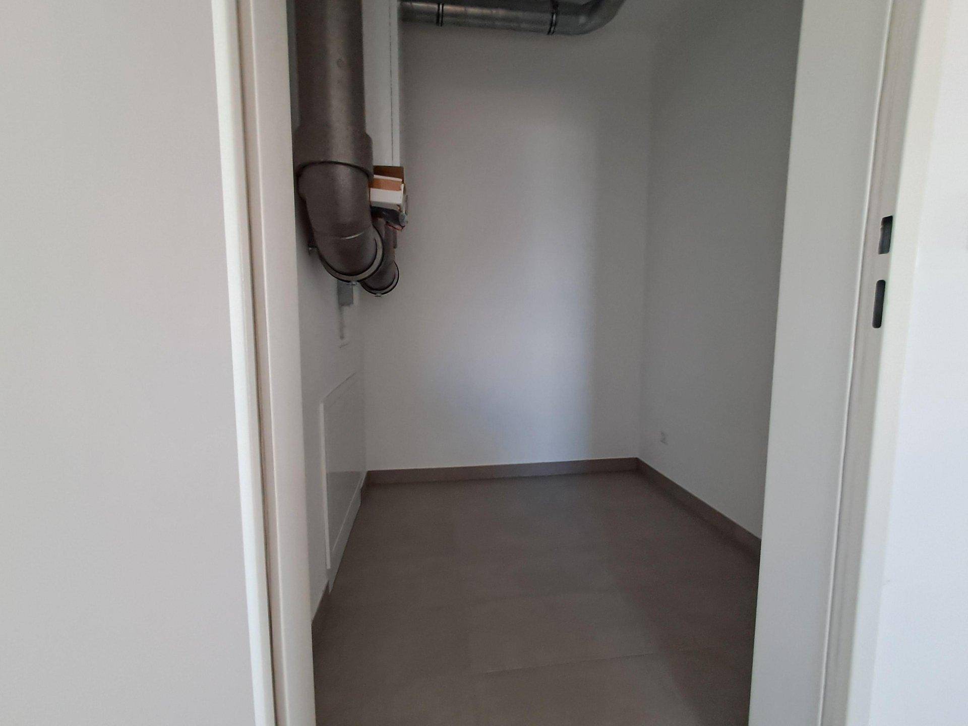Kleiner Abstellraum mit sichtbaren Rohren und grauen Fliesenboden.