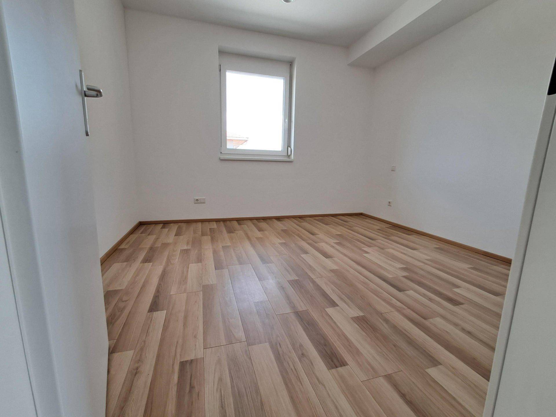 Geräumiges Schlafzimmer mit Laminatboden und einem Fenster für natürliches Licht.