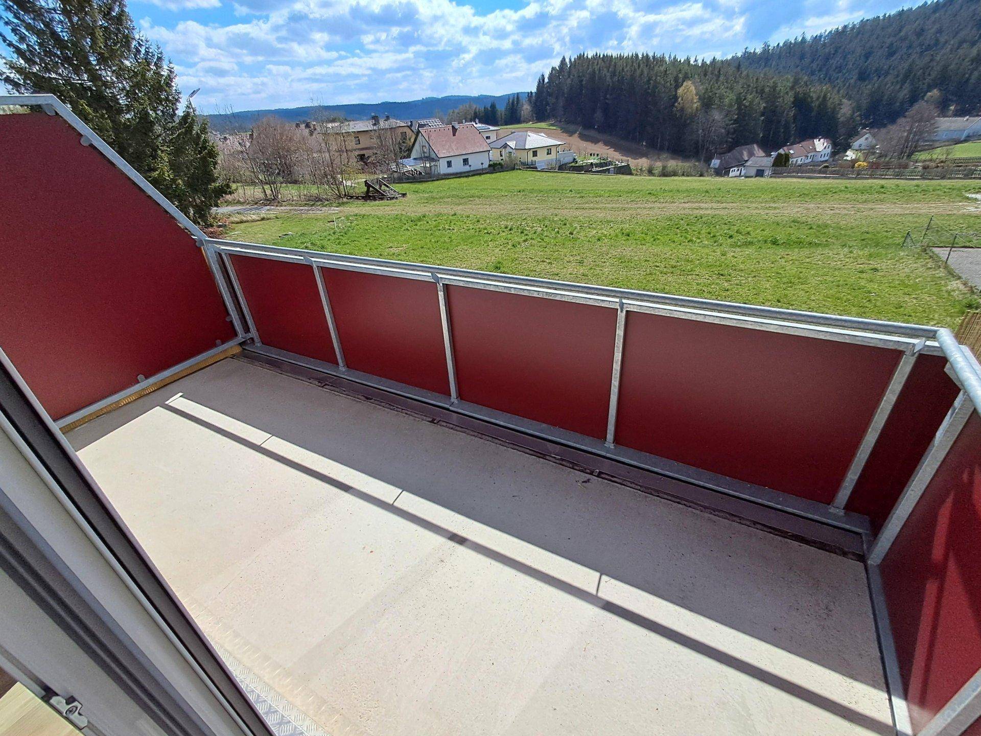 Geräumiger Balkon mit rotem Geländer und weitem Blick auf die grüne Umgebung.