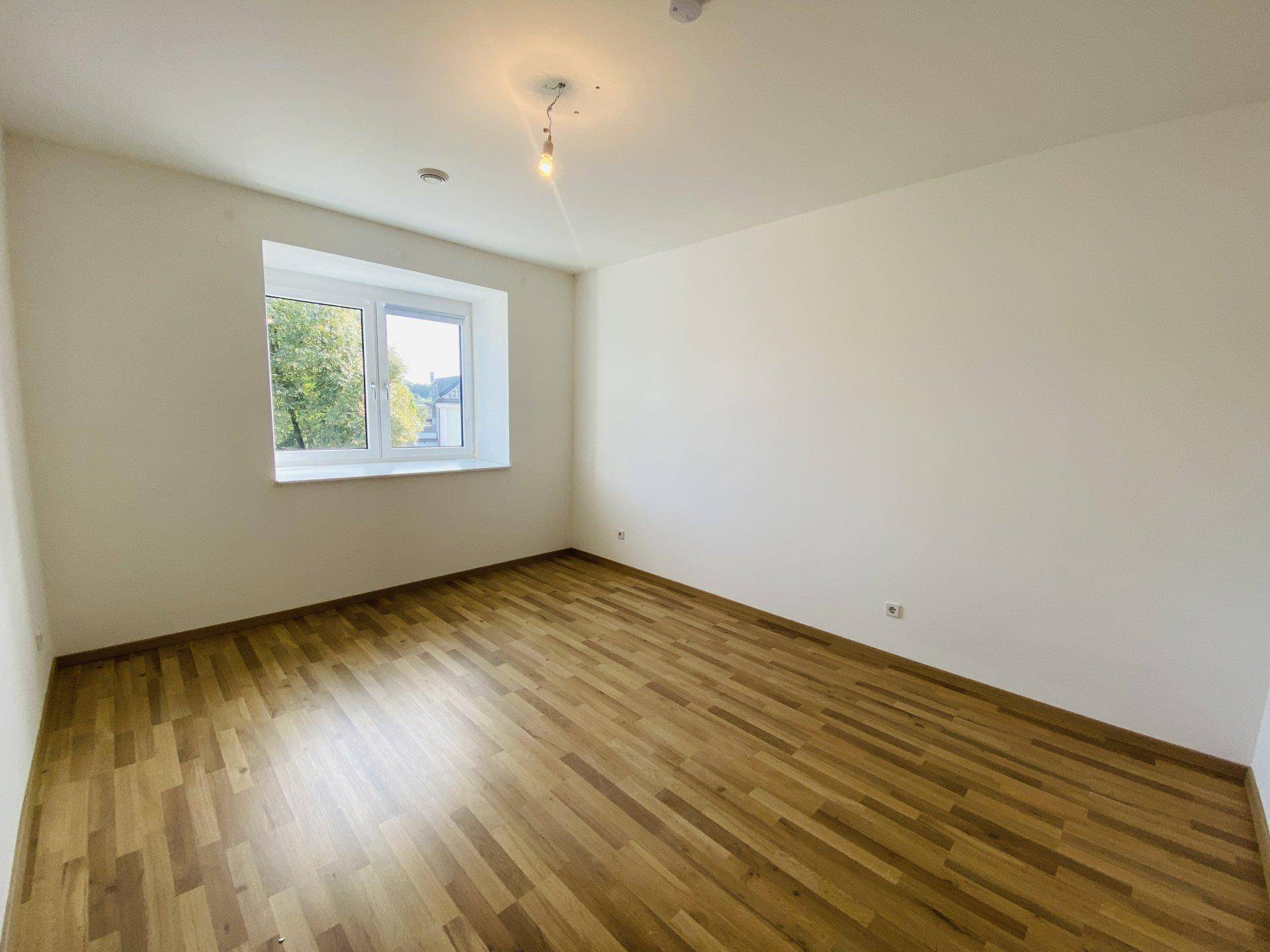 Gemütliches Schlafzimmer mit Holzparkettboden und einem Fenster, das eine ruhige Aussicht bietet.