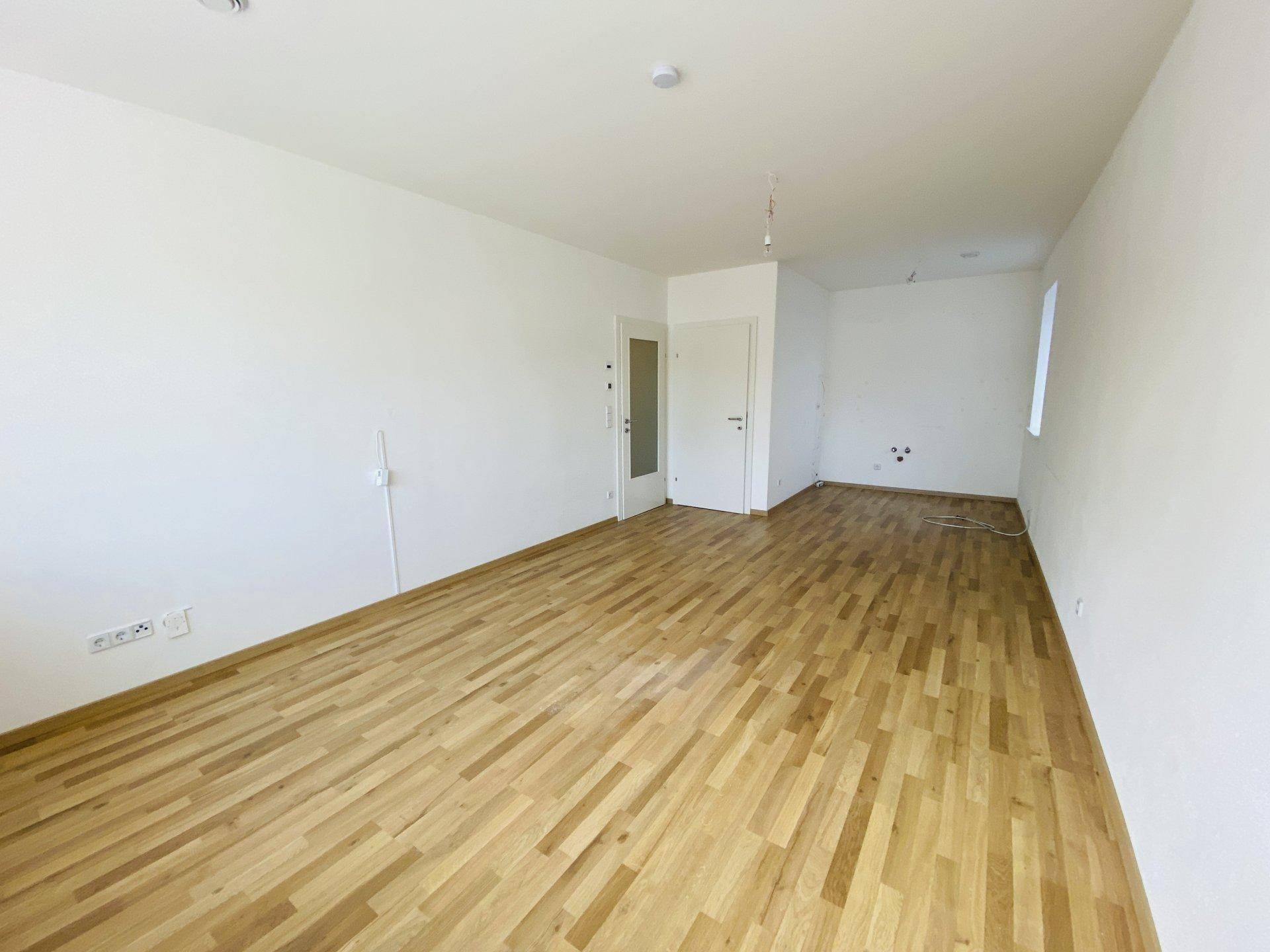 Geräumiges, leeres Zimmer mit hellem Holzparkett und weißen Wänden, bereit zum Einzug.