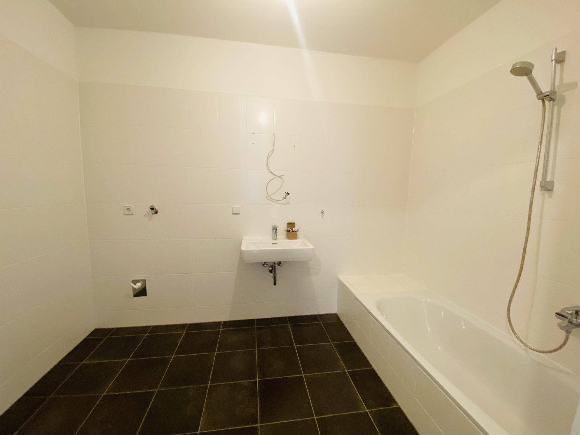 Modernes Badezimmer mit Badewanne, Waschbecken und dunklen Fliesen auf dem Boden.