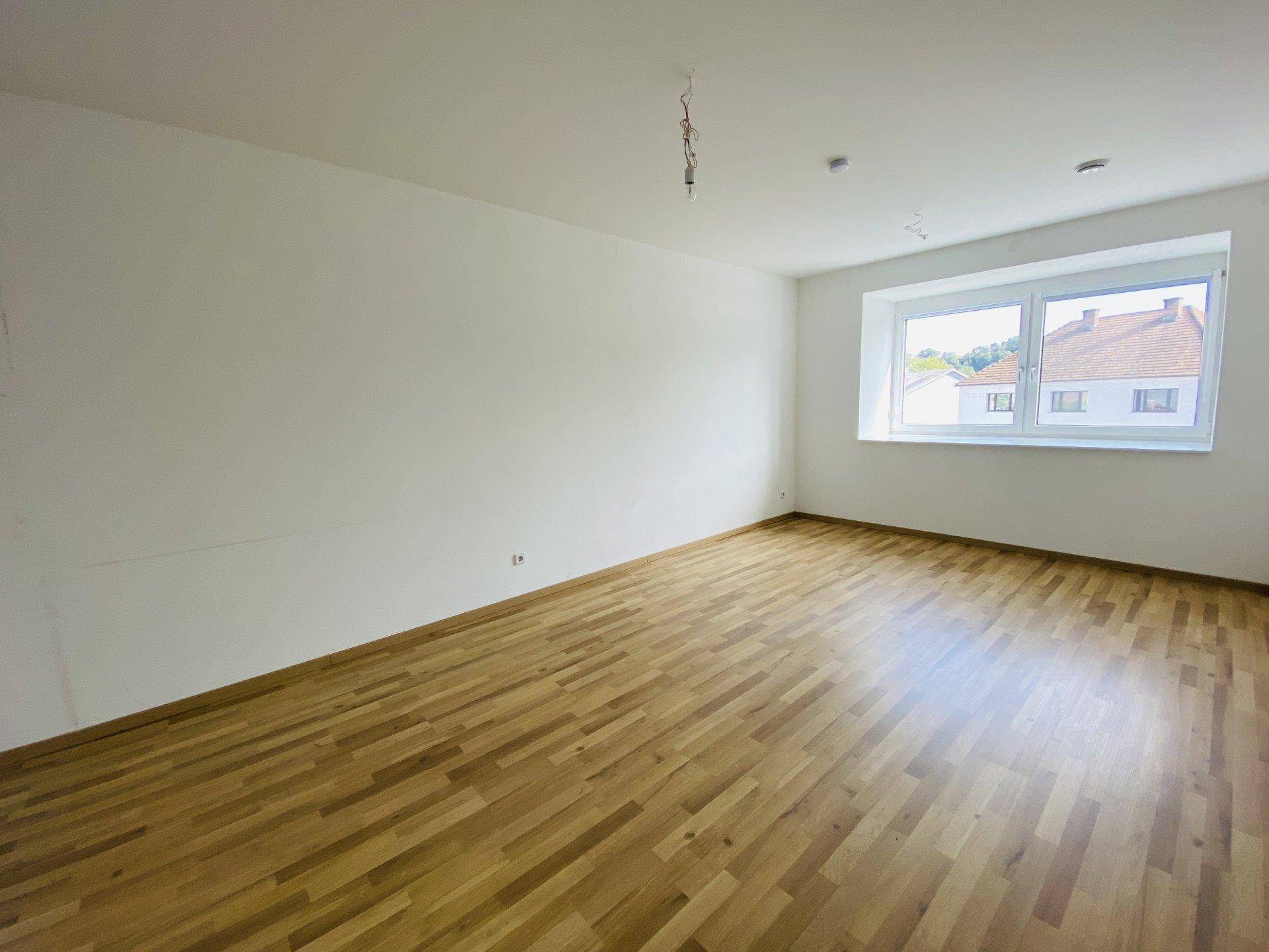 Helles Zimmer mit Holzparkettboden und großem Fenster, das viel Tageslicht hereinlässt.