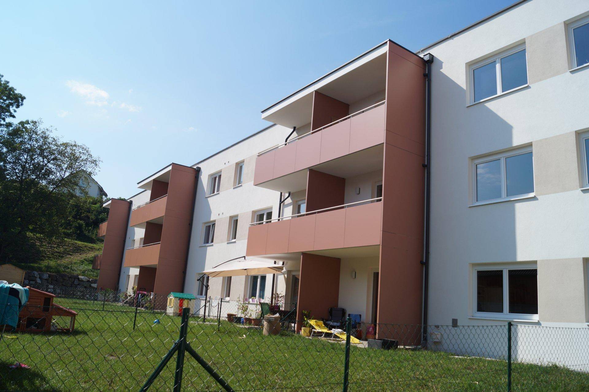 Ansicht des Mehrfamilienhauses von der Gartenseite mit Balkonen und Grünflächen.