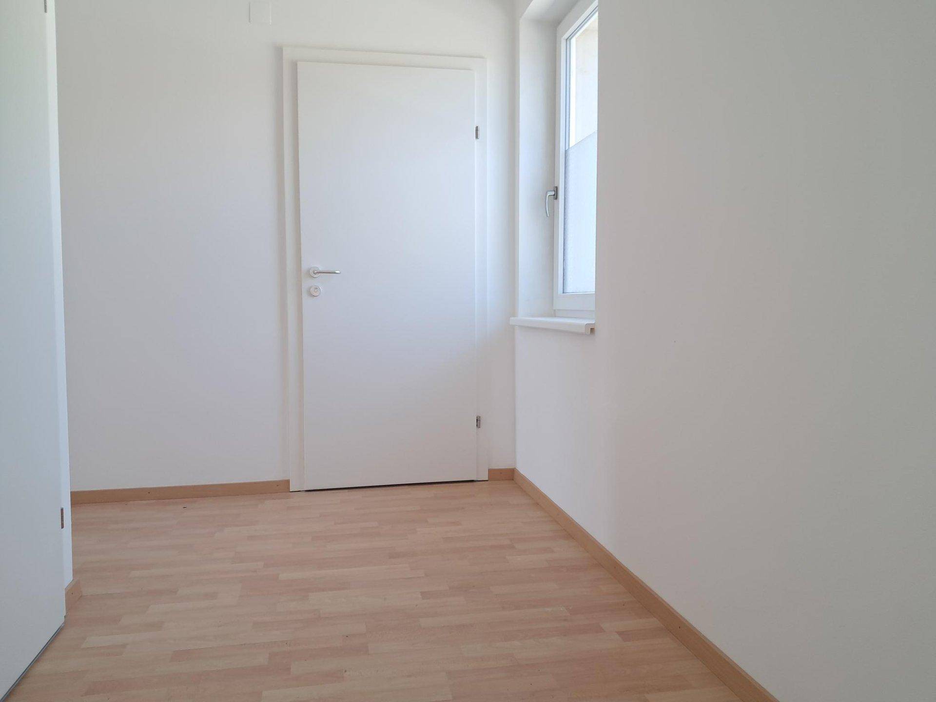 Heller, leerer Raum mit Laminatboden und einem Fenster, bereit zur individuellen Gestaltung.